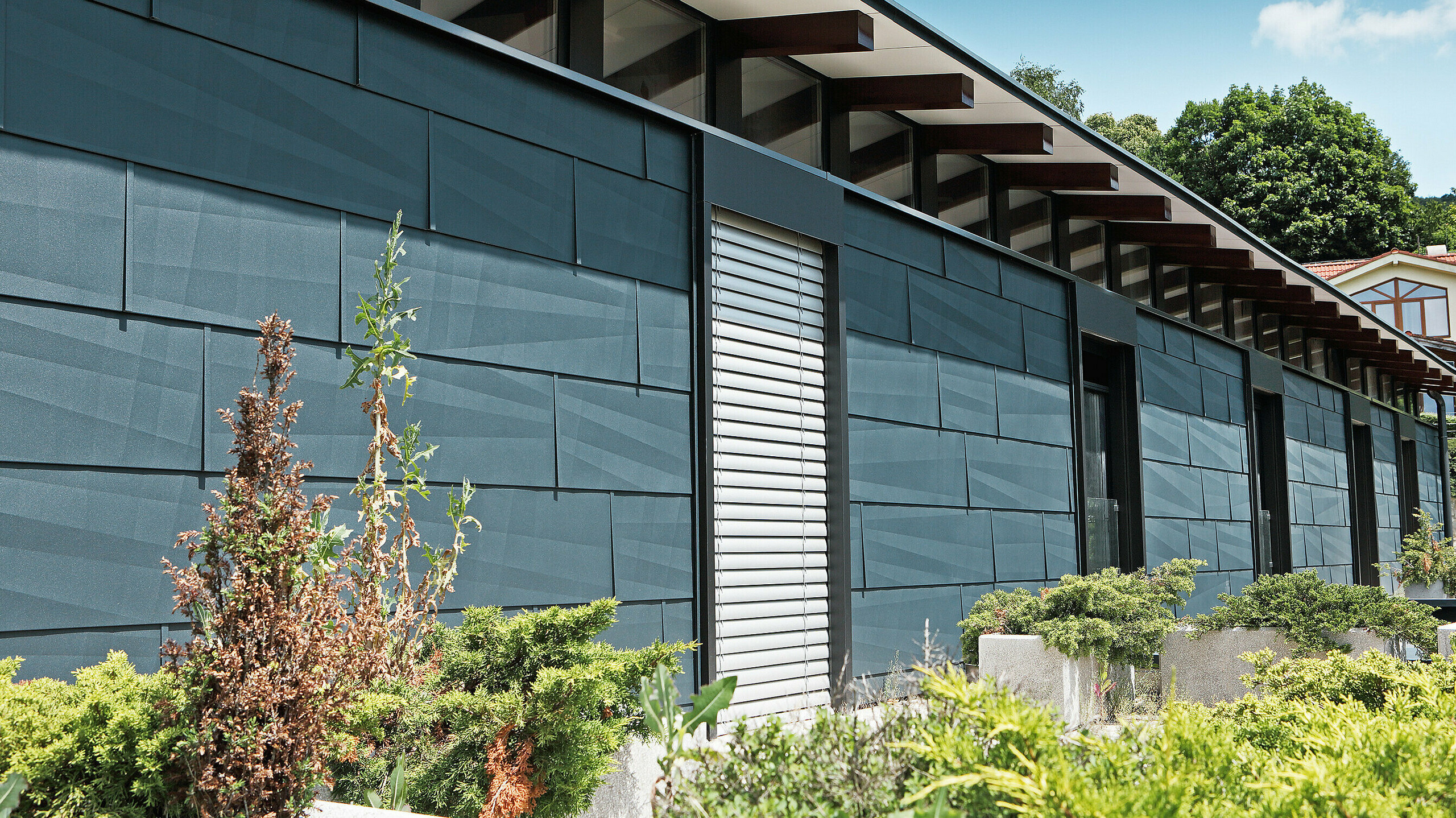 Côté exposé aux intempéries et donnant sur un jardin d’aspect moderne grâce au panneau de façade FX.12 couleur anthracite.