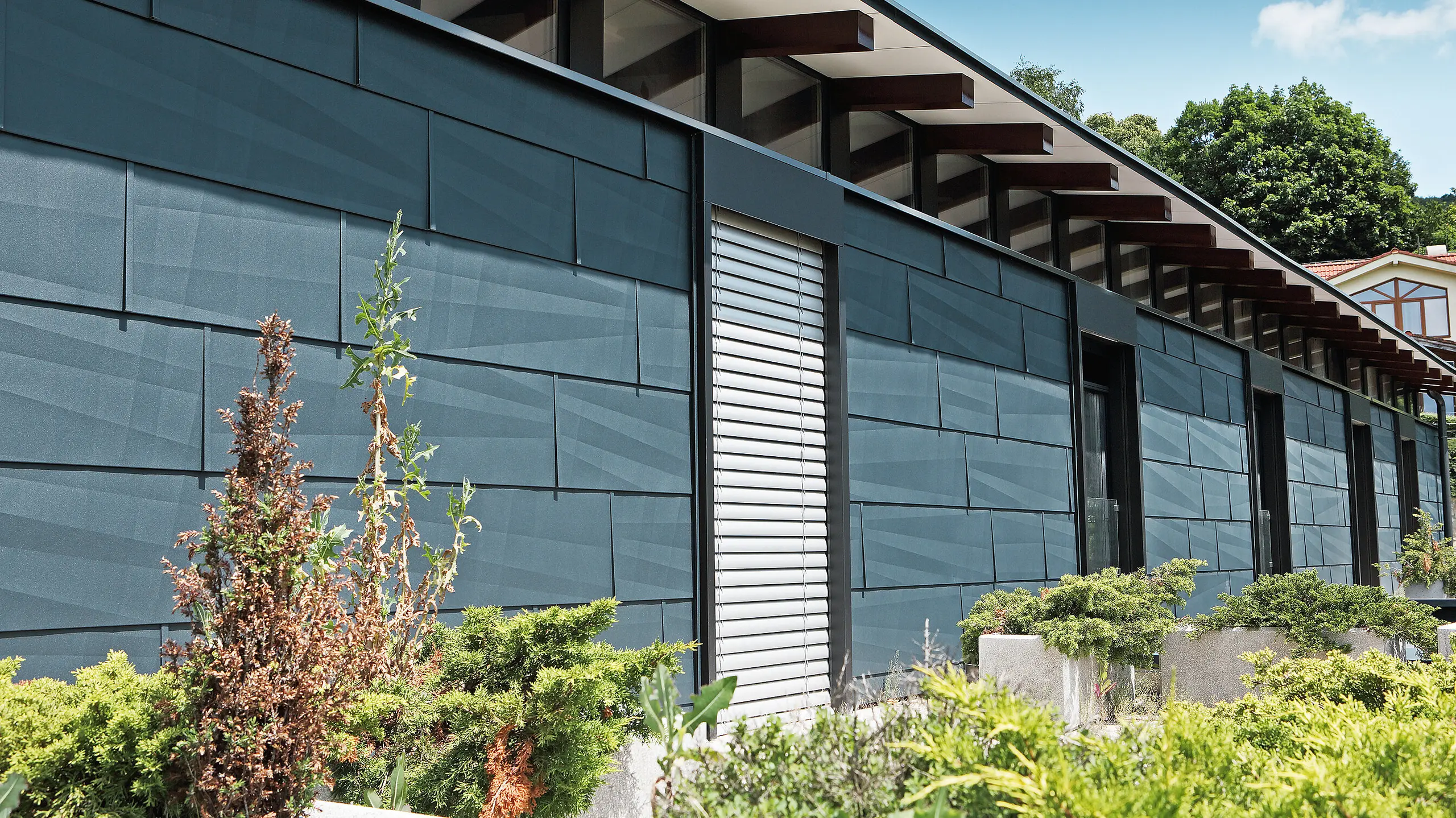 Côté exposé aux intempéries et donnant sur un jardin d’aspect moderne grâce au panneau de façade FX.12 couleur anthracite.