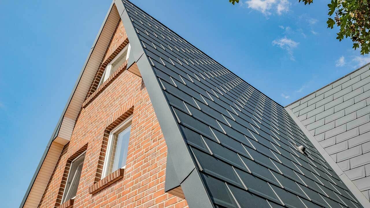 Toit à deux pans d’une maison à ossature en A, recouvert avec la tuile PREFA couleur anthracite et avec une façade en brique.