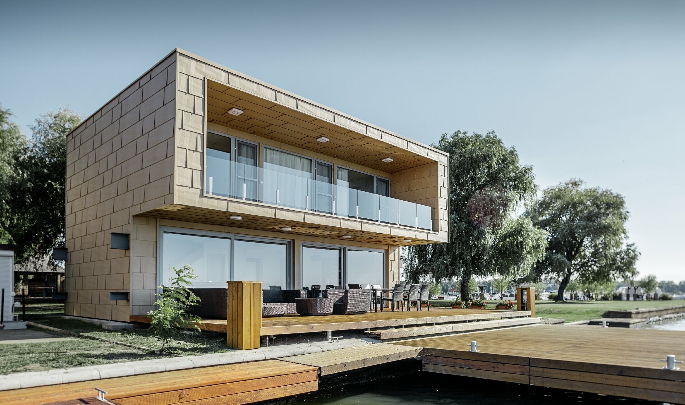 modernes Wochenendhaus mit Flachdach und großen Fensterflächen am See mit einer gekanteten Aluminiumfassade in sandbraun