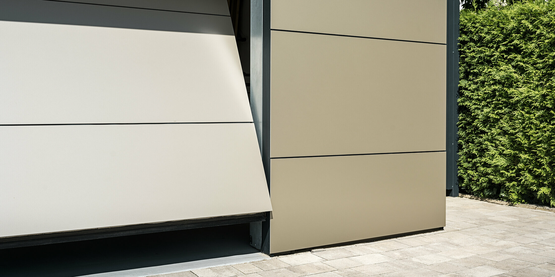 Nahaufnahme eines automatischen Garagentors. Die Garage und das automatische Garagentor sind mit bronzefarbenen Aluminium Verbundplatten verkleidet. Die präzise Verarbeitung spiegelt die Qualität der langlebigen Verbundplatten wider. Der schmale Öffnungsspalt gewährt einen kleinen Einblick in das Innere der Garage.