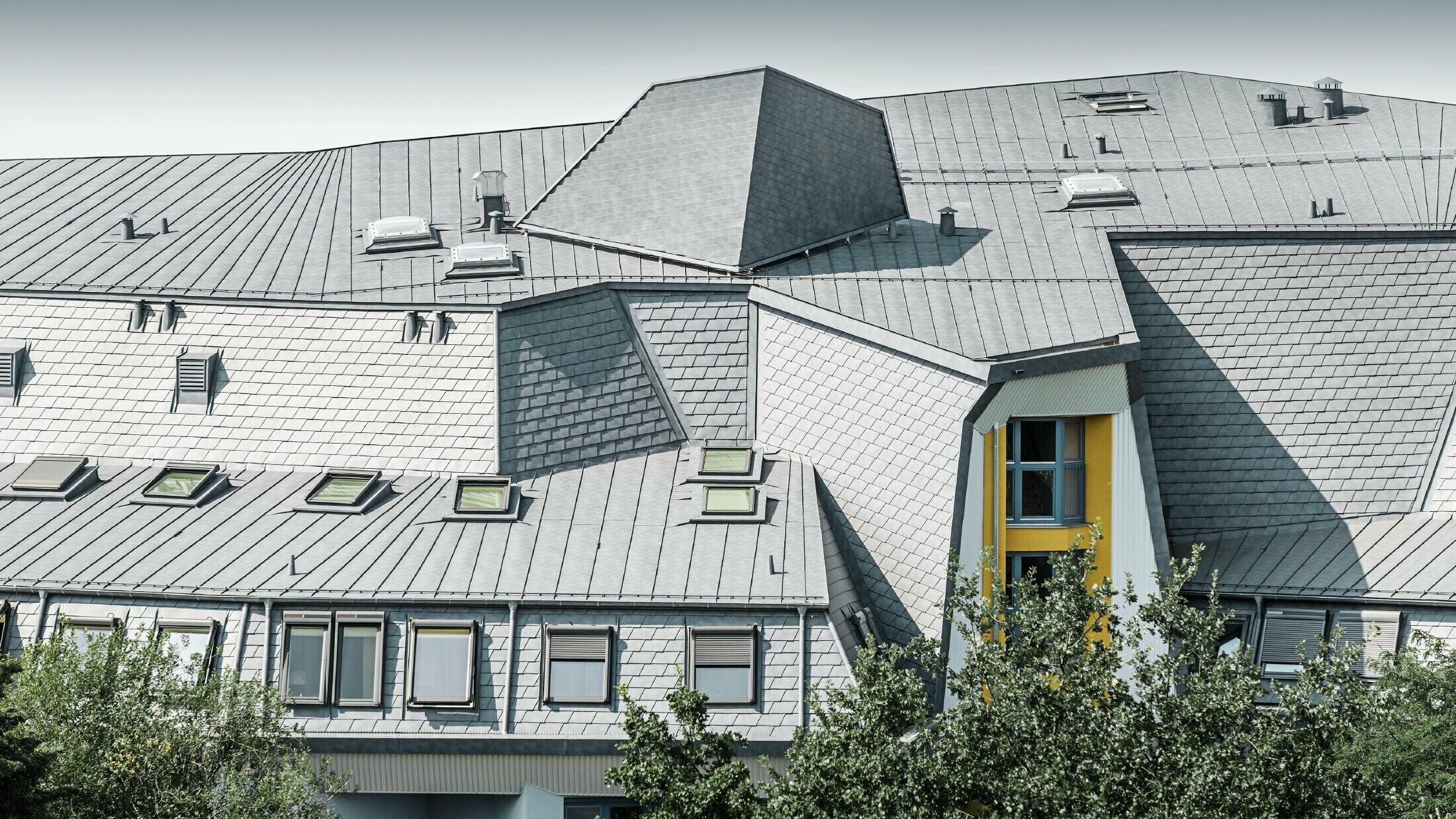 Toiture complexe avec lucarnes et pentes sur l’établissement Haus Aja Textor-Goethe, recouvert de bardeaux de toiture et Prefalz PREFA couleur gris pierre