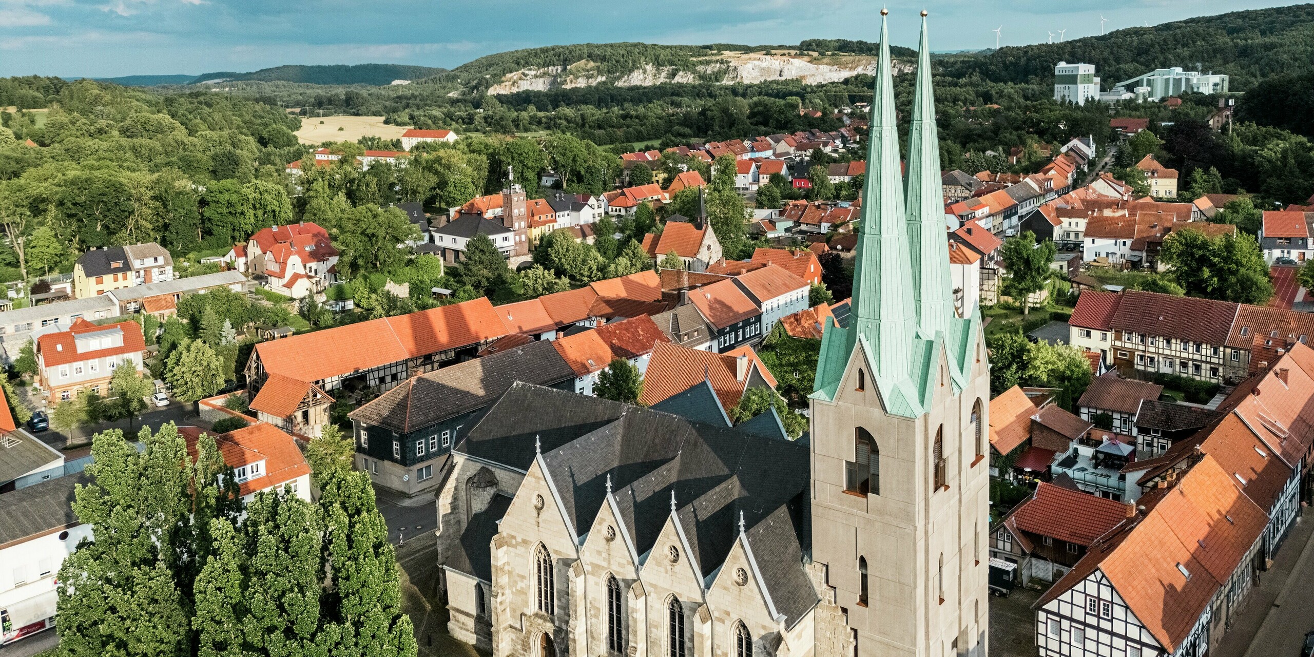 Images aériennes de l'église Saint-Jean d'Ellrich, en Thuringe, avec ses flèches remarquables en PREFALZ vert de gris P.10. La toiture moderne en aluminium apporte une touche architecturale distinctive au cœur historique de la ville. Entourée de toits de tuiles rouges et de maisons à colombages, cette toiture durable et sans entretien s'intègre harmonieusement et avec assurance au paysage urbain.