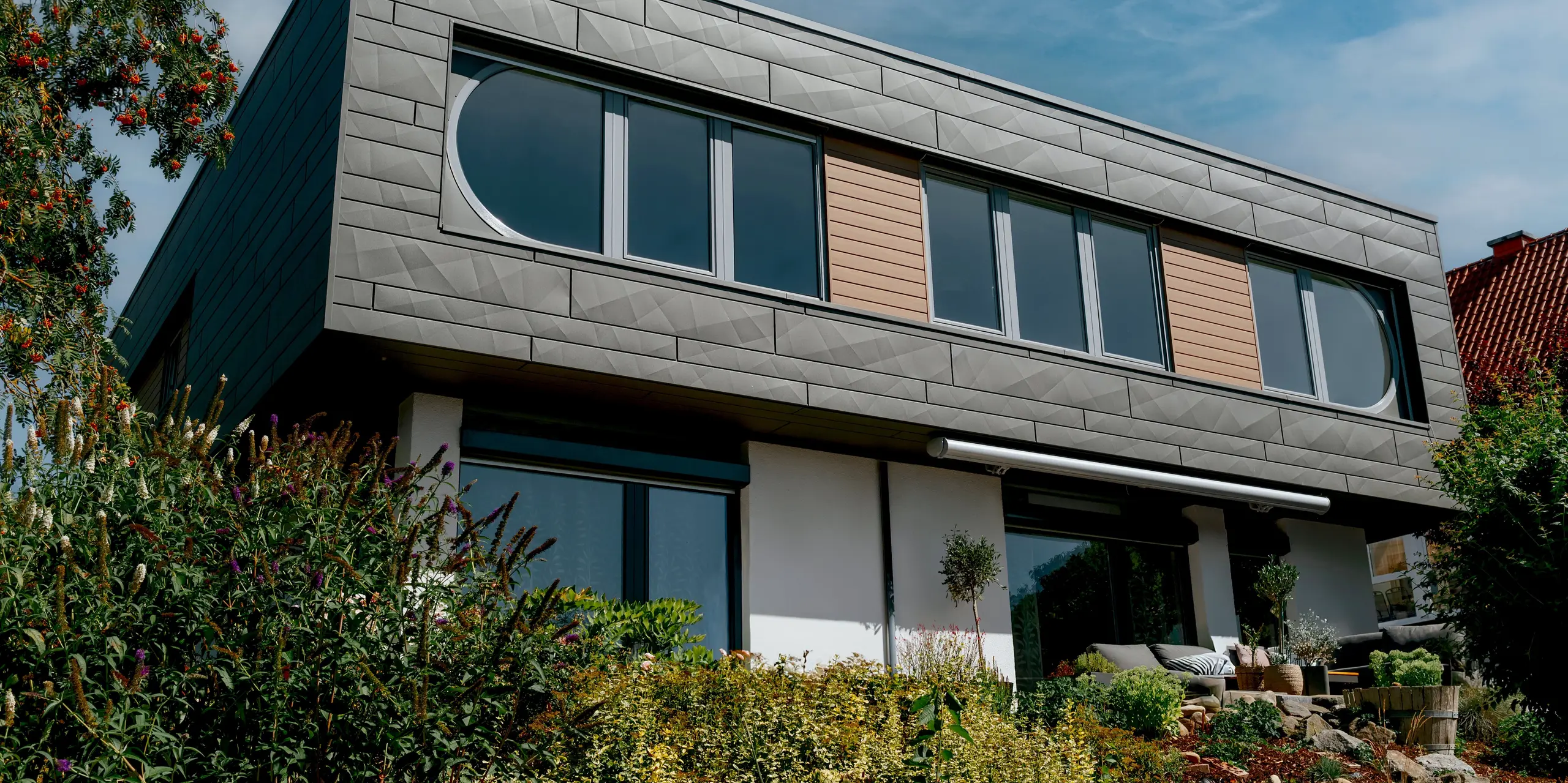 Architektonisches Detail eines modernen Einfamilienhauses in Marksuhl mit PREFA Aluminiumfassade: Die PREFA Siding.X Paneele in P.10 Dunkelgrau bilden eine elegante, strukturierte Gebäudehülle mit markanter Linienführung. Fensterbänder und Siding-Elemente in Walnuss braun setzen warme Kontraste. Die robuste Aluminiumfassade überzeugt durch Langlebigkeit, Witterungsbeständigkeit und zeitlose Gestaltung.