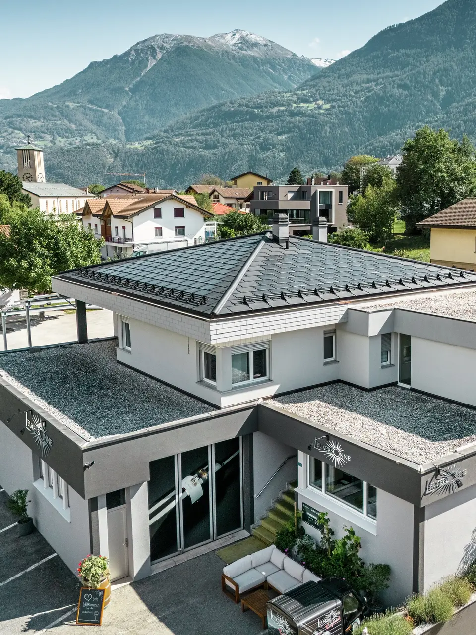 Das elegante PREFA Dach aus Aluminium verleiht der Weinkellerei Leukersonne in Susten (CH) ein modernes Erscheinungsbild und bietet optimalen Schutz vor Witterungseinflüssen. PREFA Solardachplatten sorgen für eine nachhaltige Energiegewinnung ohne das Erscheinungsbild des Zeltdaches zu beeinträchtigen. Abgerundet wird die Dachlandschaft durch PREFA Dachplatten R.16. Das erste Obergeschoss und der restliche Teil des zweiten Obergeschosses sind mit einem begehbaren Kiesbelag versehen. 