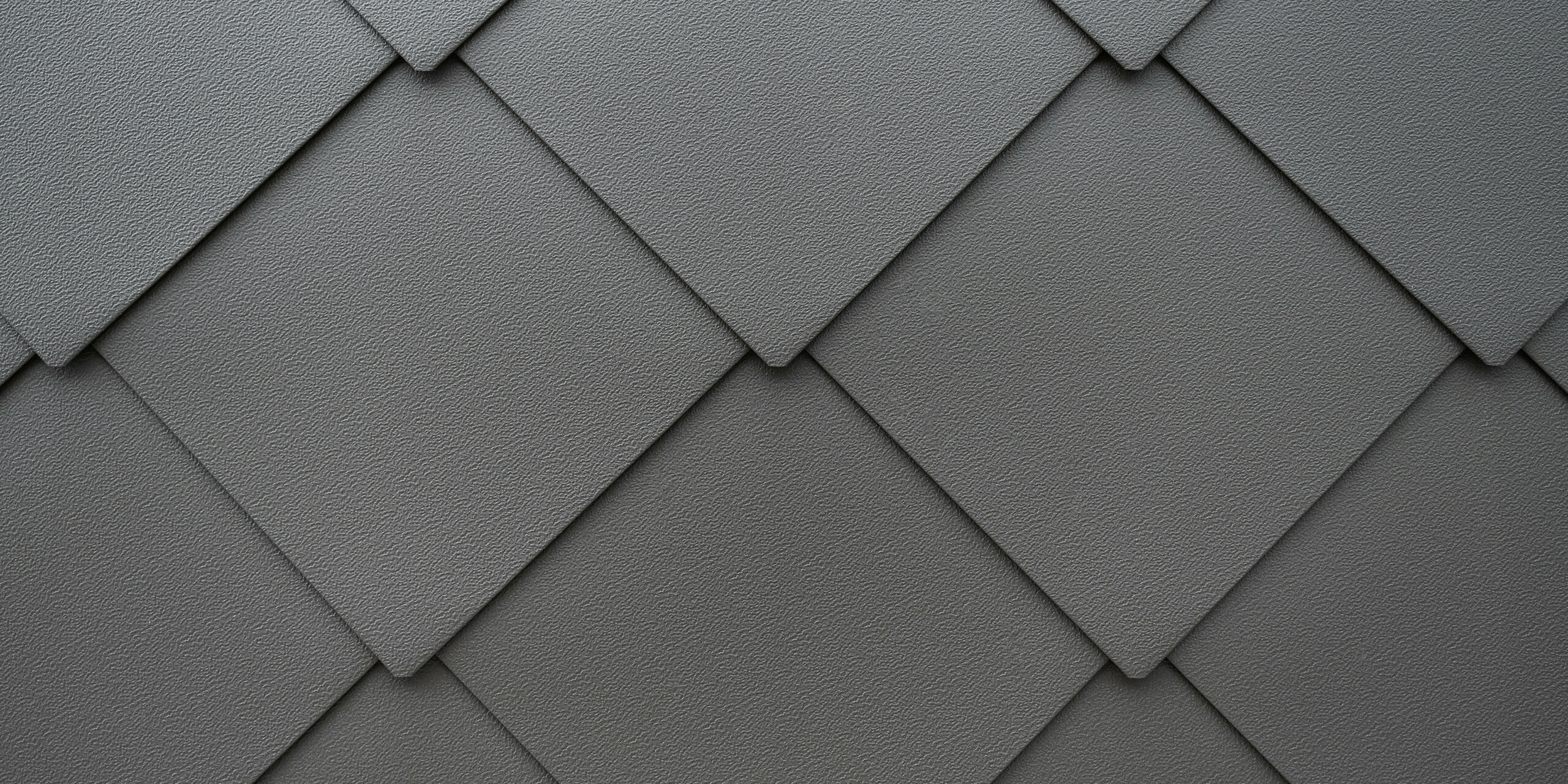 Detailaufnahme der texturierten Oberfläche eines PREFA Fassadensystems aus Aluminium. Die harmonische Anordnung der PREFA Wandrauten 44x44 erzeugt ein klares, geometrisches Muster, das Eleganz und moderne Architektur widerspiegelt, betont durch die subtile Farbgebung und die präzise Verarbeitung. Das widerstandsfähige Blech bietet dem Reihenhaus in Kaltern, Südtirol, Schutz vor winterlichen Bedingungen.