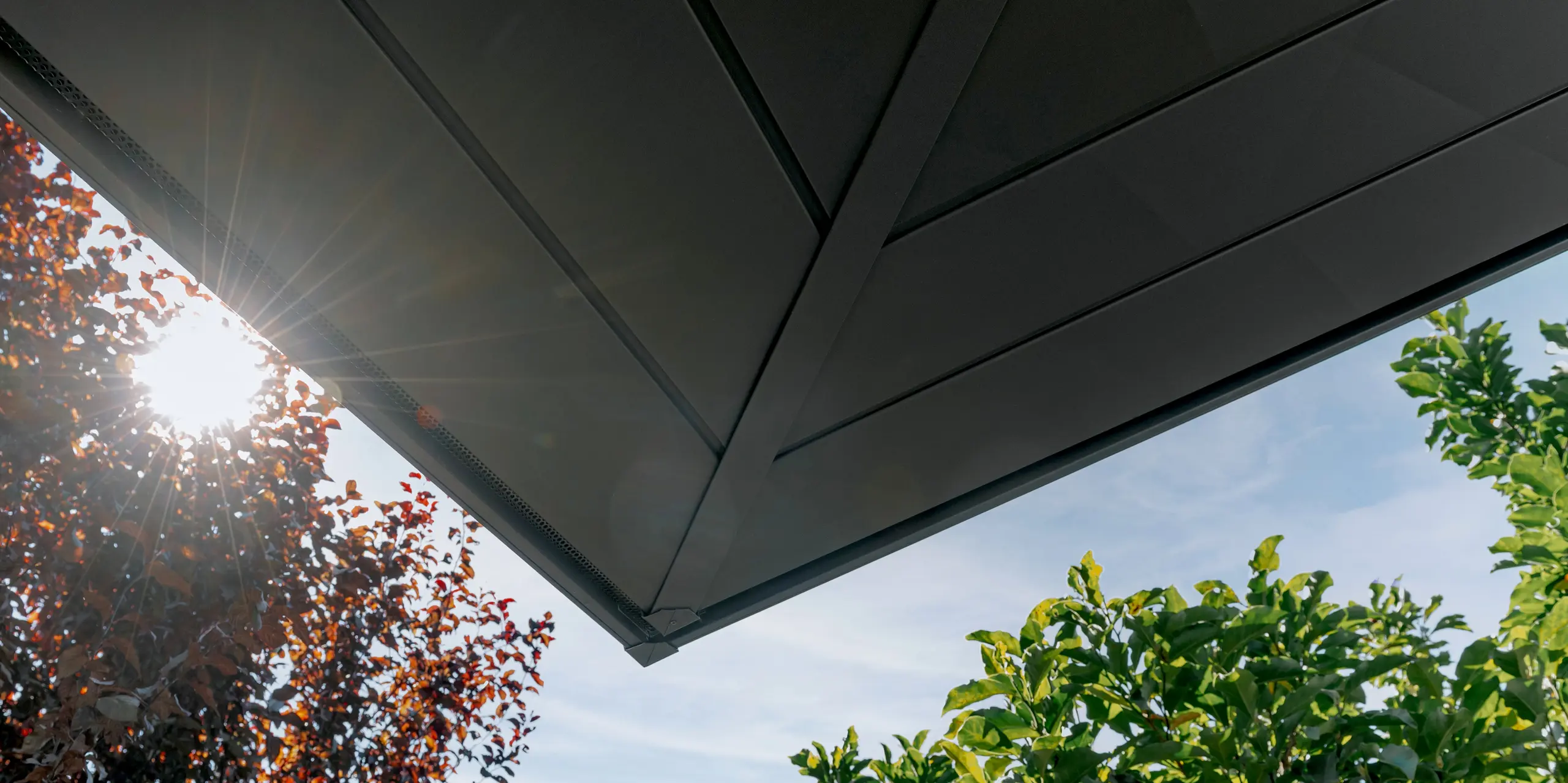 Detailaufnahme der Untersicht des auskragenden Obergeschosses mit moderner PREFA Aluminiumverkleidung: Die präzise gefügten PREFA Siding.X Paneele in P.10 Dunkelgrau setzen markante Akzente. Die langlebige, witterungsbeständige und wartungsarme Aluminiumfassade überzeugt durch klare Linien, hochwertige Verarbeitung und eine elegante Optik im Zusammenspiel mit der Natur.