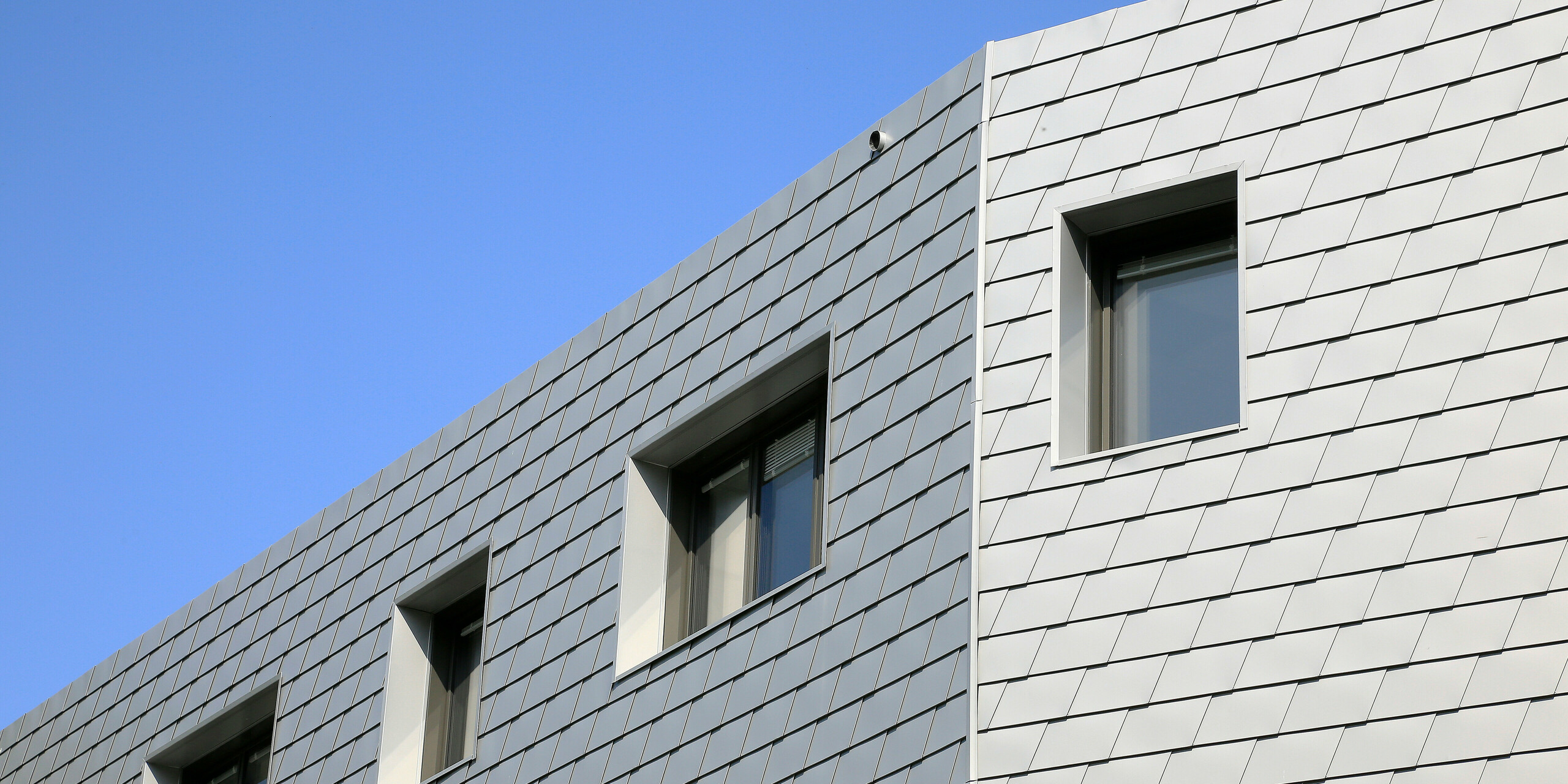 Die Gebäudekante auf der Rückseite des Gesundheitszentrums in Le Landreau wird von kleinformatigen Fassadenschindeln aus Aluminium umhüllt