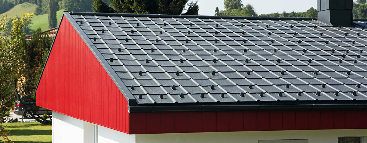Revêtement de pignon rouge avec Sidings PREFA en aluminium, posés verticalement. Le toit a été recouvert de tuiles PREFA couleur P.10 anthracite.