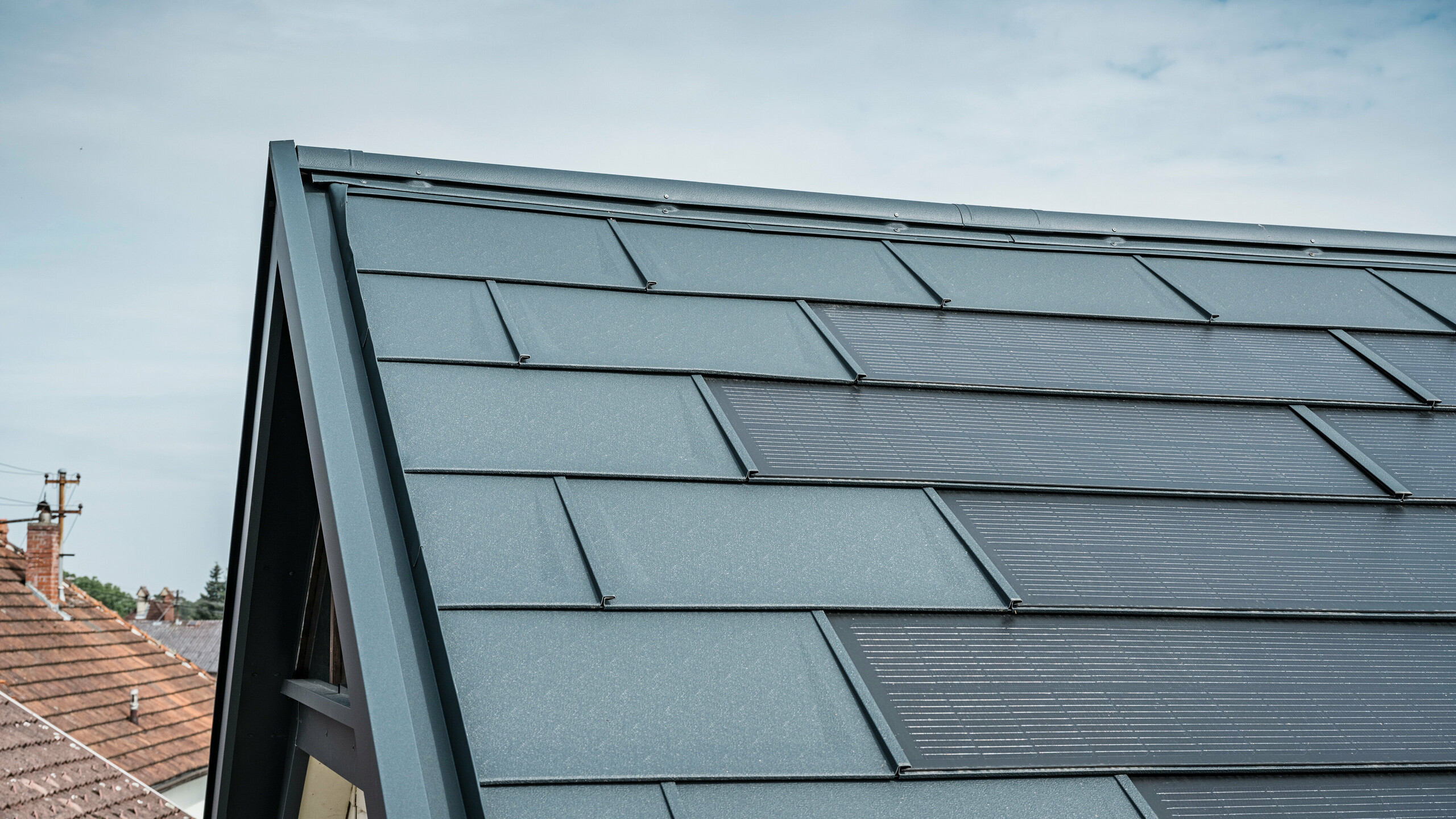 Vue détaillée du toit d'une maison équipée de la tuile solaire innovante PREFA. Les tuiles avec cellules photovoltaïques intégrées sont présentées dans un élégant anthracite. La surface homogène s'intègre parfaitement dans le toit et assure ainsi un aspect moderne et épuré. Le système de toiture innovant permet une utilisation efficace de l’énergie sans compromettre l’esthétique.