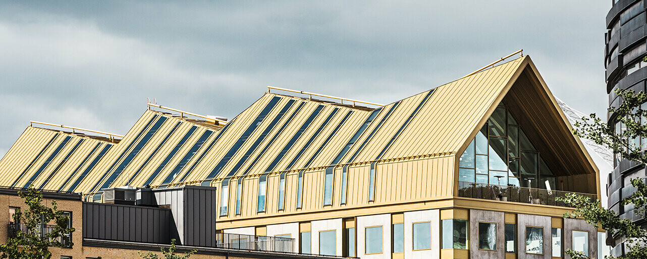 seitliche Frontansicht des Gebäudes in Malmö eingedeckt mit dem Dachsystem PREFALZ in der Sonderfarbe Jaisalmer Gold