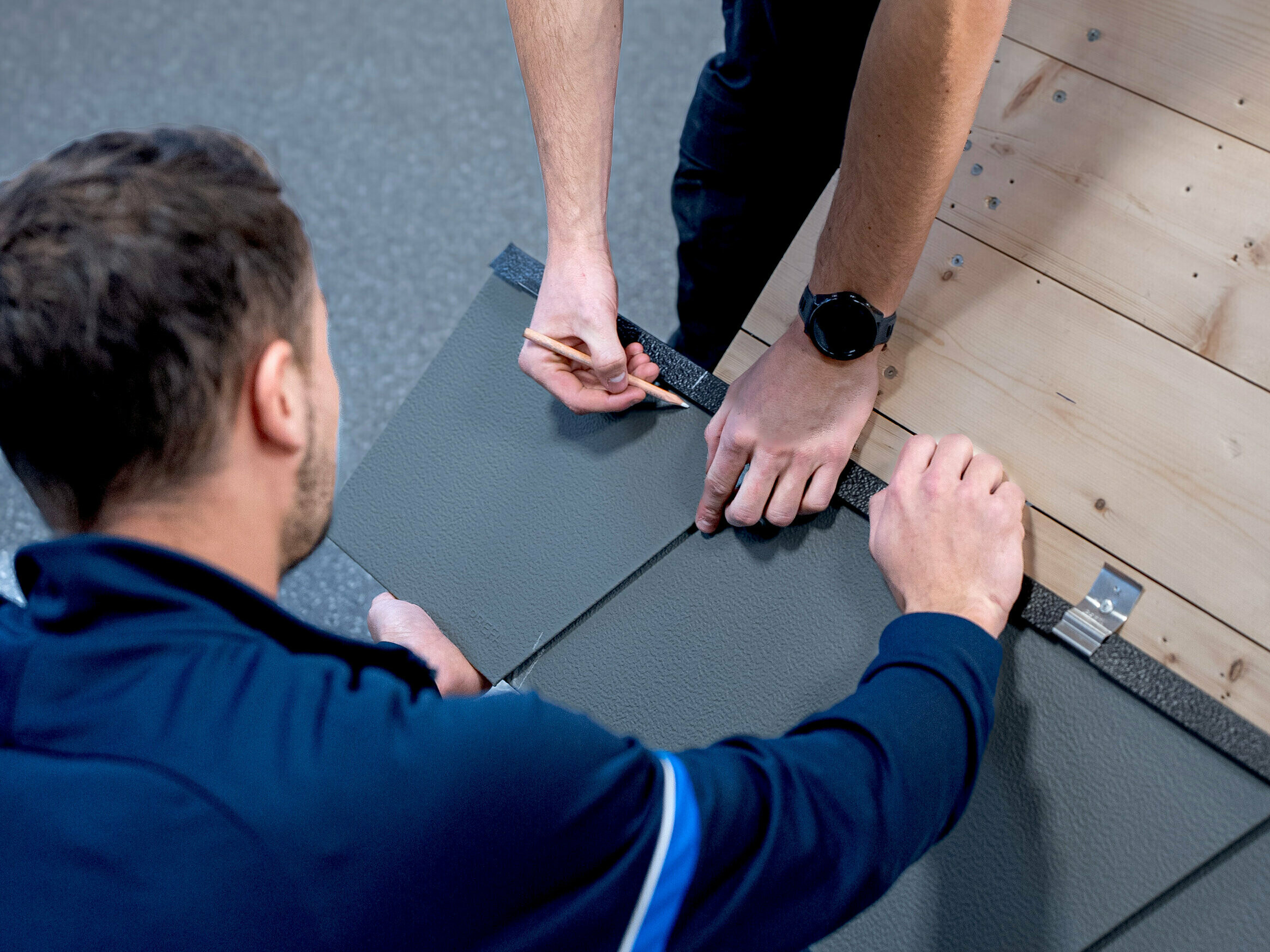 Un istruttore PREFA mostra ad un partecipante alla PREFA Academy il metodo corretto di posa dei prodotti PREFA.