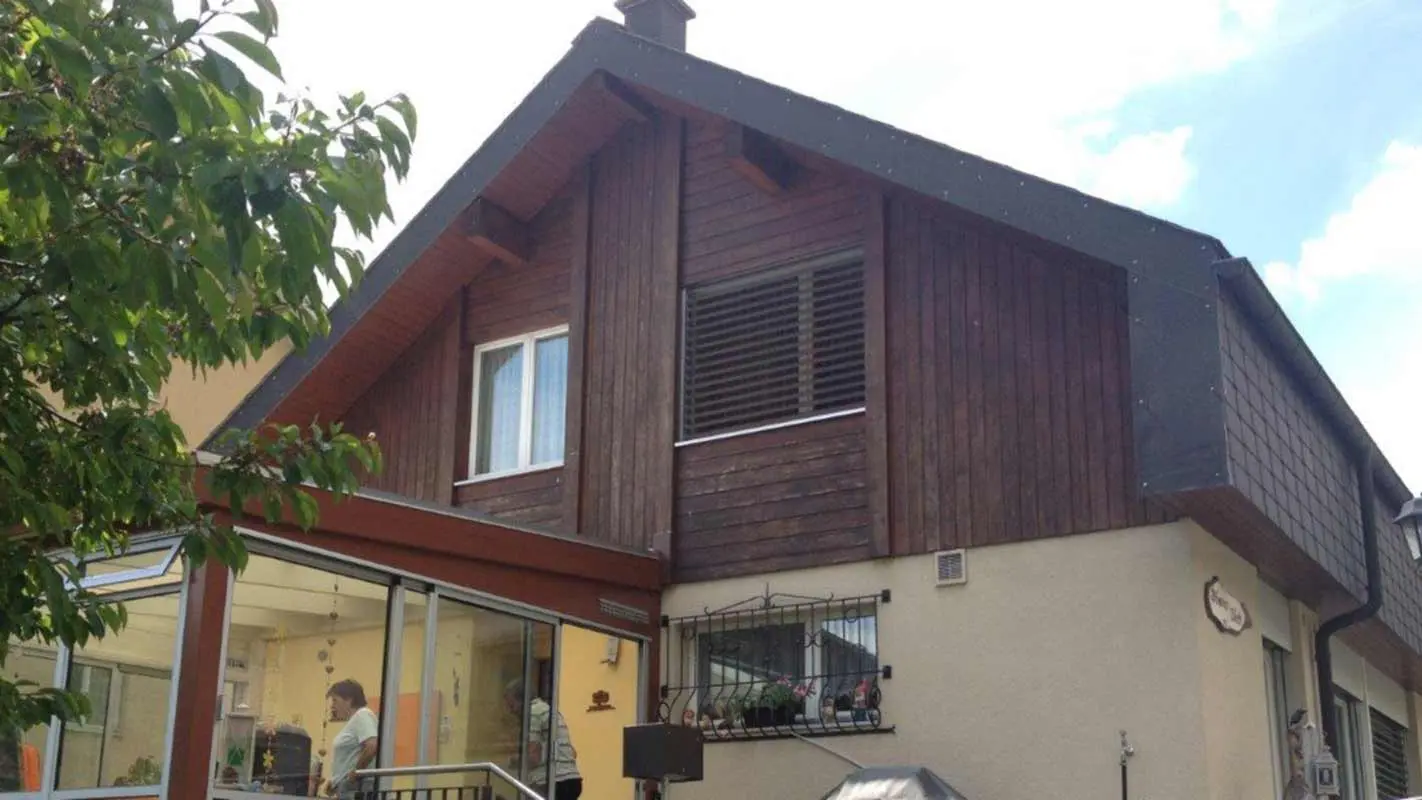 Casa prima della ristrutturazione della facciata con doghe di rivestimento PREFA con effetto legno, il timpano è ancora rivestito con legno deteriorato