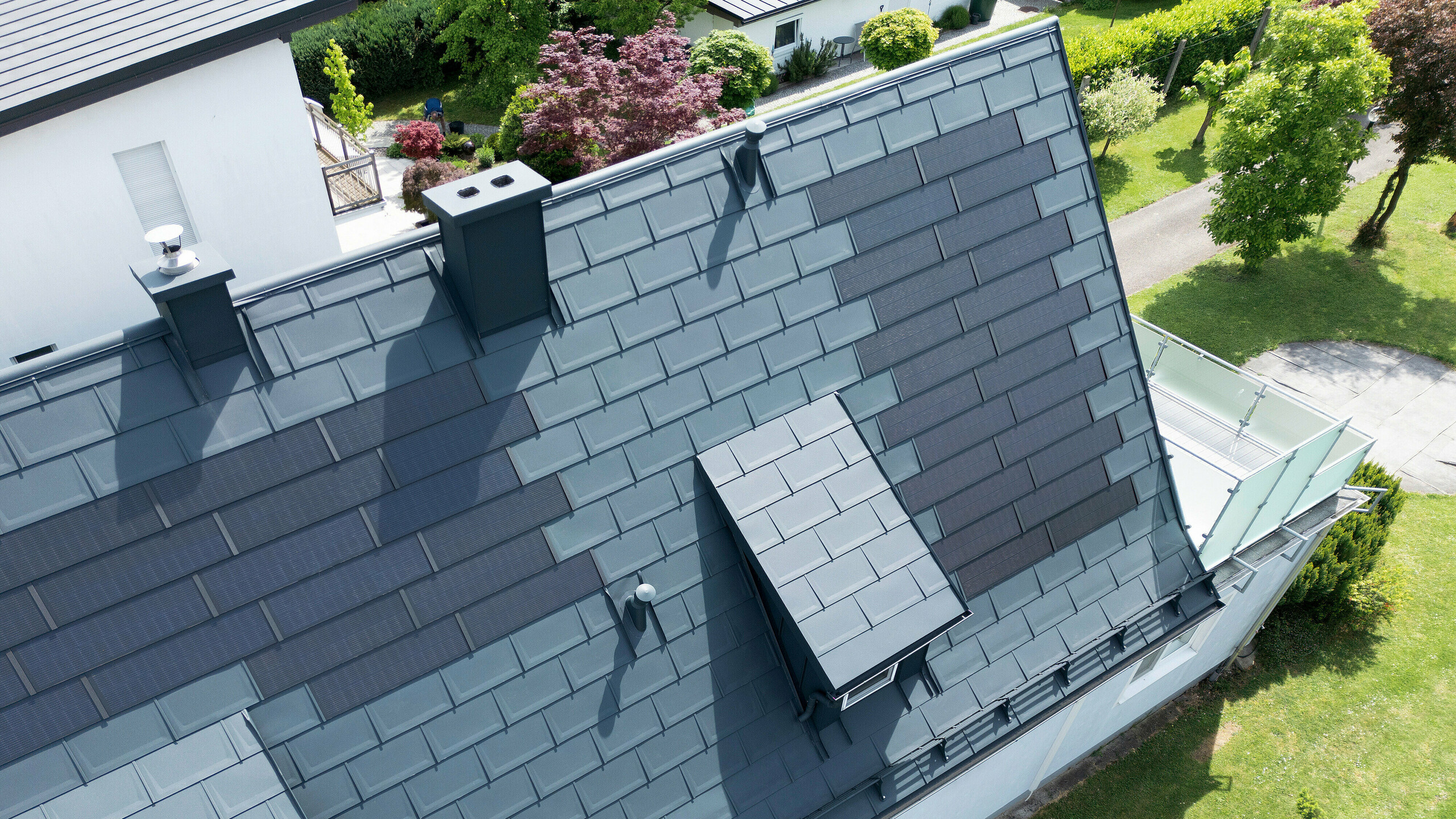 Komplette Dachsanierung eines Einfamilienhauses in Leonding mit PREFA Solardachplatten in Anthrazit. Die Nahaufnahme aus der Vogelperspektive zeigt das Dach nach der Sanierung, ausgestattet mit integrierten Solarmodulen. Diese innovative Lösung kombiniert ästhetische Integration und nachhaltige Energiegewinnung. Die langlebigen und witterungsbeständigen Materialien von PREFA sorgen für eine moderne und energieeffiziente Architektur, die den neuesten Standards für nachhaltiges Bauen entspricht.