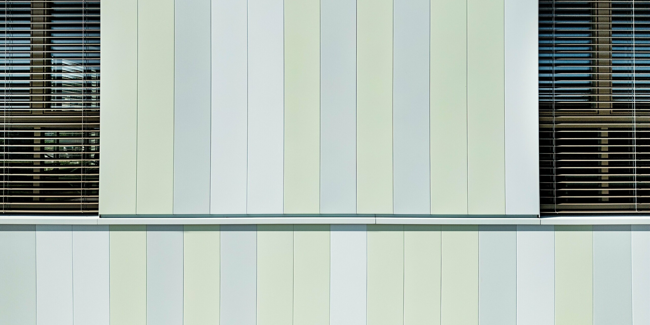 Die Fassade der AHS Reininghaus in Graz beeindruckt durch die stilvolle Kombination von PREFA Sidings in Sonderfarben. Die vertikalen Aluminiumprofile in sanften Grün- und Weißtönen verleihen dem Gebäude ein modernes, frisches Erscheinungsbild. Besonders auffällig sind die perfekt abgestimmten Fensterrahmen und Jalousien, die das lichtdurchflutete Design der Fassade ergänzen. Die Verwendung von PREFA Produkten sorgt für eine besonders langlebige, pflegeleichte und wetterbeständige Oberfläche, die gleichzeitig ästhetische Akzente setzt. Diese moderne Fassadengestaltung trägt nicht nur zur optischen Aufwertung des Gebäudes bei, sondern sorgt auch für nachhaltige Energieeffizienz und Schutz vor Umwelteinflüssen.