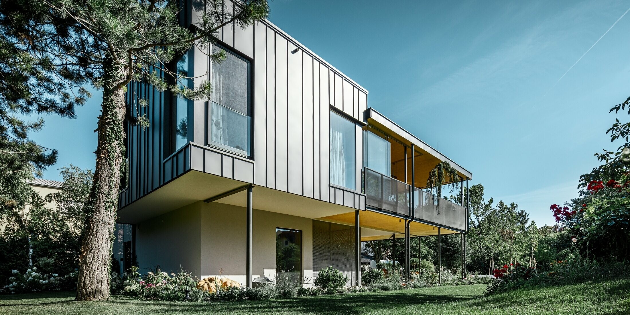 modernes Einfamilienhaus, ähnlich einem Baumhaus umgeben von einem großen Garten mit vielen Bäumen mit einer dezenten Winkelstehfalzfassade in schwarzgrau von PREFA
