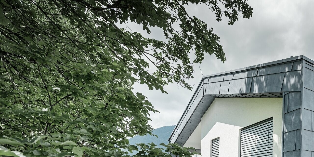 Structure moderne d’un bâtiment d’habitation avec toit à deux pans et sans avancée de toit ; l’habillage de façade a été réalisé avec le panneau de façade FX.12 PREFA couleur gris pierre.