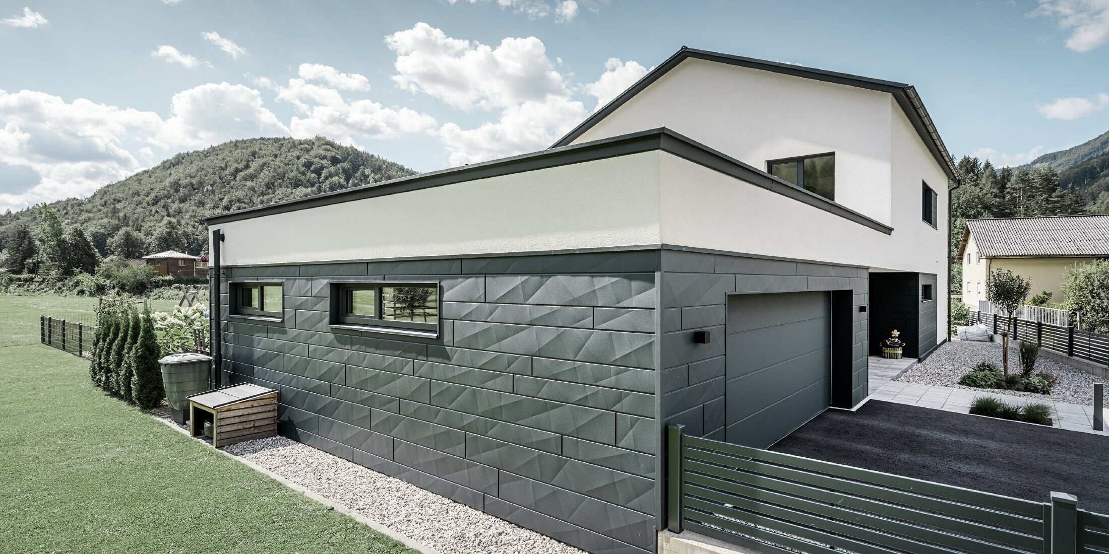 Maison individuelle moderne et garage avec façade en Siding.X couleur P.10 anthracite. Elle est située dans un environnement rural.