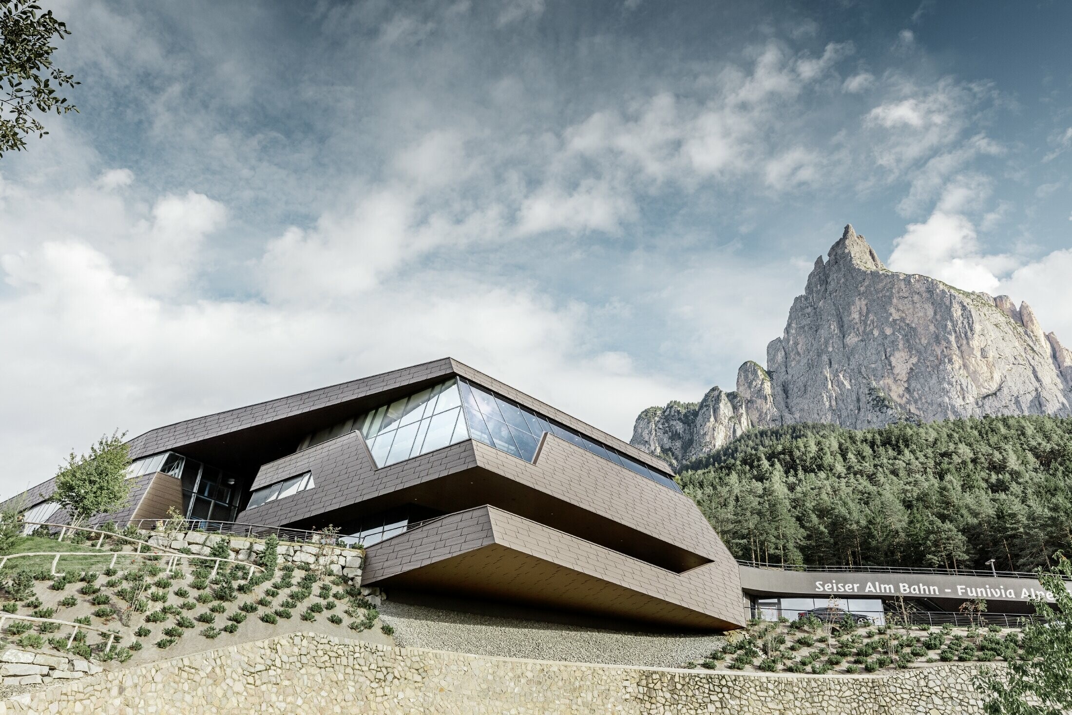 Stazione a valle della cabinovia dell'Alpe di Siusi, simile alle dolomiti sullo sfondo con bordi e superfici irregolari con una facciata in alluminio marrone di PREFA