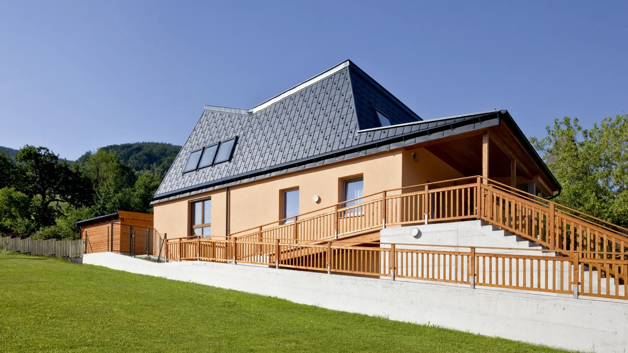 Maternelle avec façade en crépi orange et toiture à pans inclinés, recouverte de tuiles PREFA P.10 anthracite ;