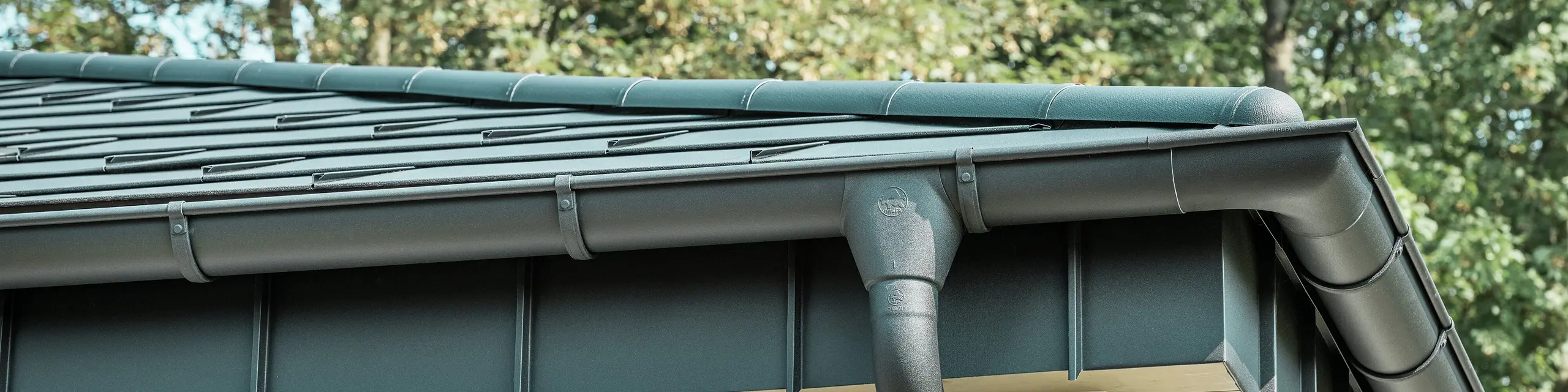 Detailansicht der PREFA Dachentwässerung eines Bungalows in Rommerskirchen. Die hochwertige Saumrinne und das Ablaufrohr in P.10 Schwarz bieten eine sichere Dachentwässerung bei Regen. Die langlebigen PREFA Aluminiumprodukte verbinden Funktionalität mit modernem, elegantem Design.