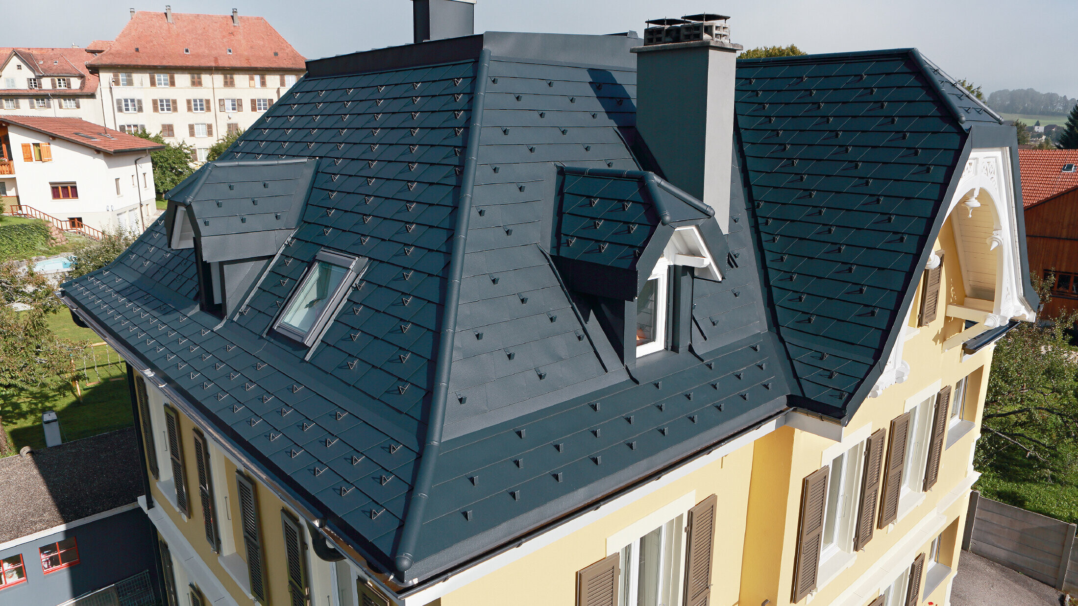 Villa in Svizzera, il tetto ha molti compluvi e piccoli abbaini, il tetto è coperto con scandole di alluminio PREFA in P.10 antracite.