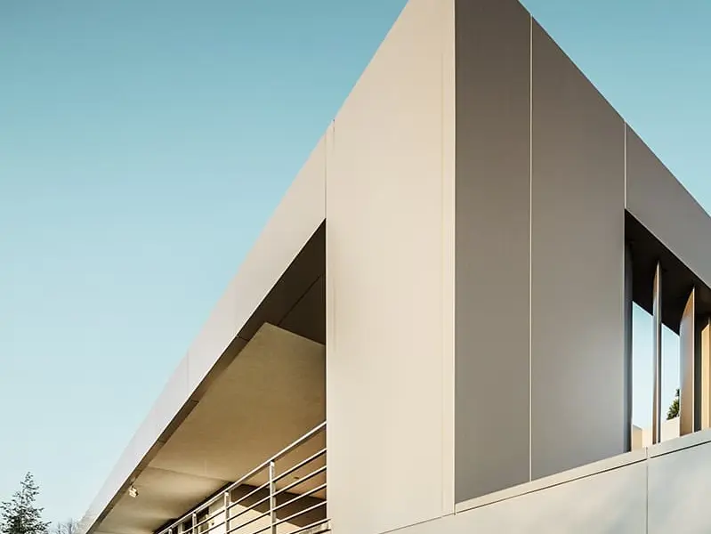 Rückansicht, unten Holzterrasse, vorne bronzefarbene Fassade, überdachte Terrasse im ersten Stock mit Metallgeländer