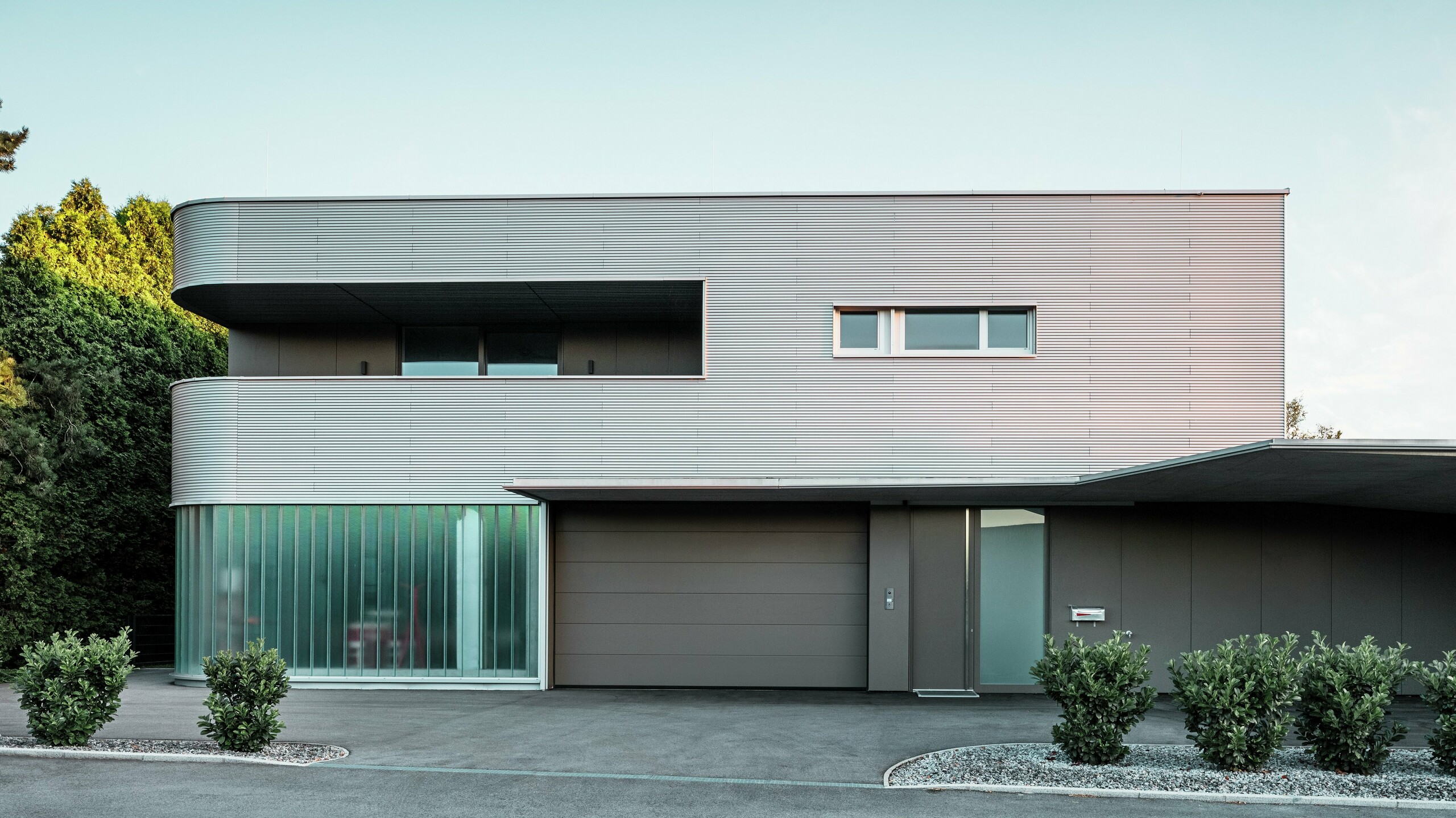 Maison moderne avec façade en aluminium naturel PREFA profil sinus et garage baigné de lumière naturelle.