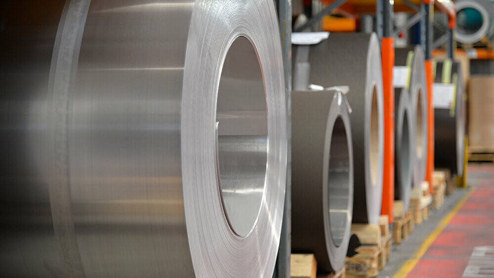Bobines d’aluminium ("coils") sur palettes en bois : au premier plan, un rouleau en aluminium naturel et derrière, d’autres bandes et feuilles d’aluminium.