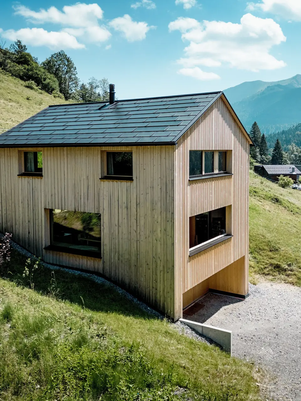 Perchée au-dessus de la vallée, la maison Immi se dresse telle un monolithe de bois épuré sur le versant ensoleillé d’Ebnit. La façade sobre en sapin blanc et le toit solaire PREFA noir créent un contraste saisissant avec l’immensité du paysage alpin. Les tuiles solaires intégrées et les R.16 en P.10 Noir produisent de l’énergie solaire, résistent aux conditions météorologiques alpines et garantissent une toiture durable et harmonieuse.