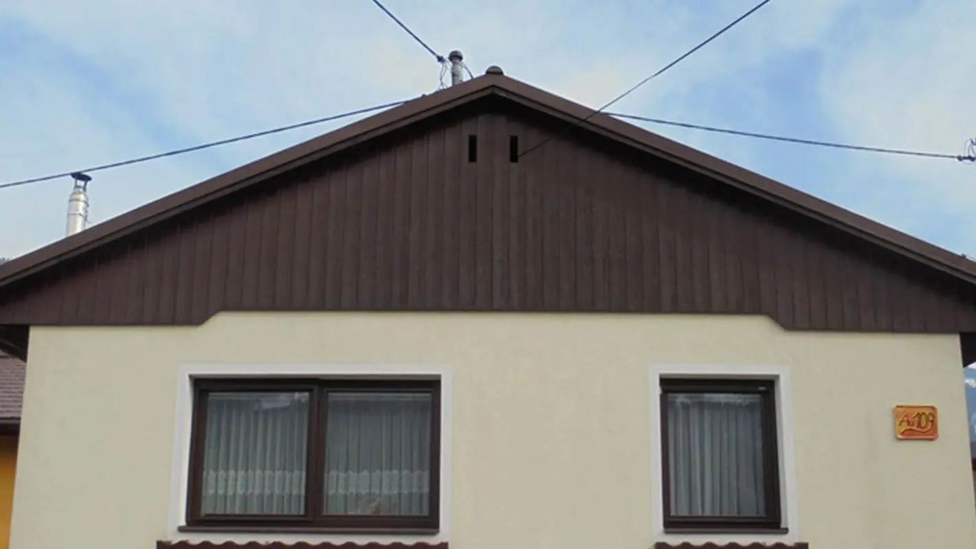 Prima della ristrutturazione della facciata del timpano con doghe di rivestimento PREFA, facciata intonacata gialla e legno deteriorato