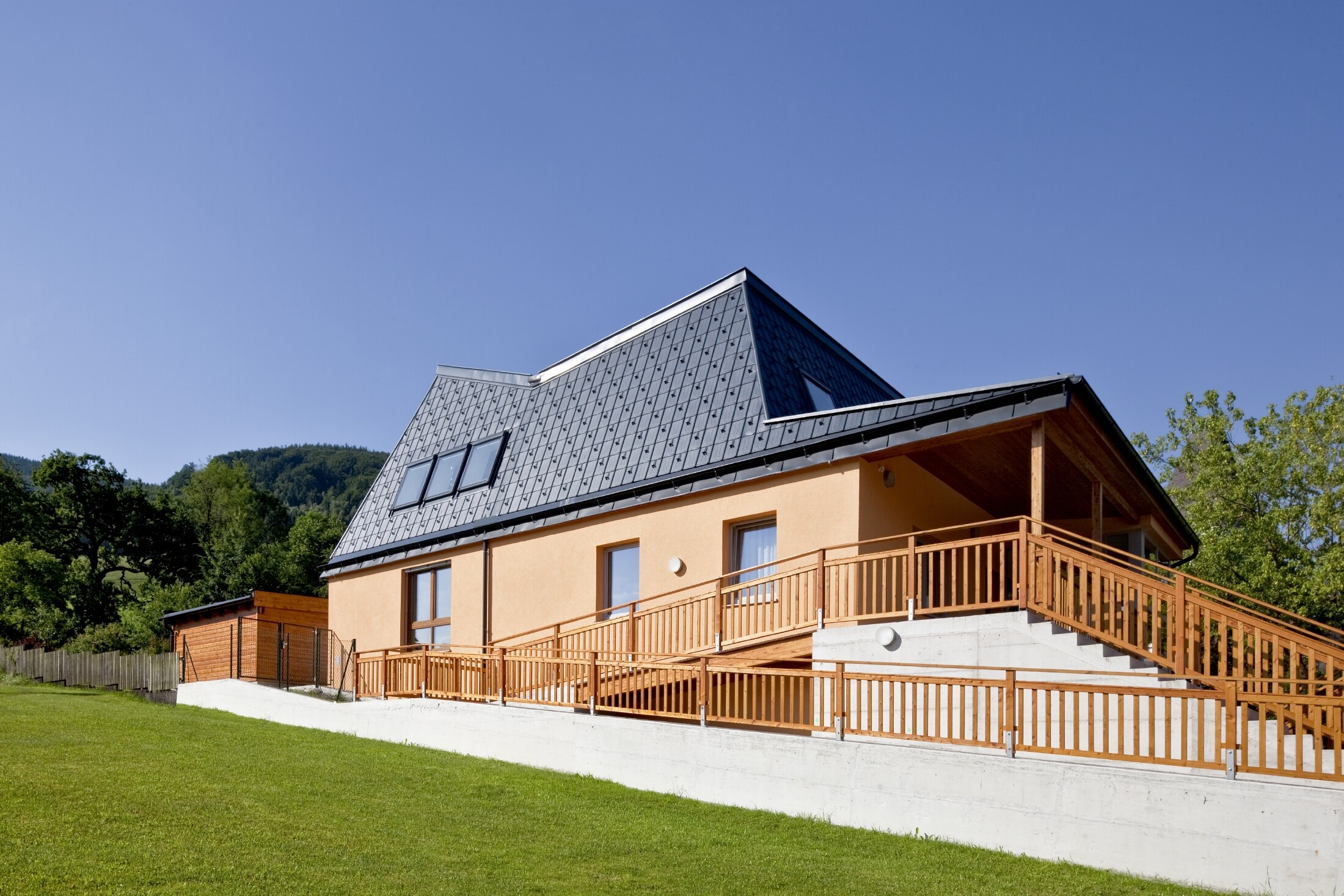 Kindergarten mit oranger Putzfassaade und verwinkeltem Dach, gedeckt mit der PREFA Dachplatte in P.10 Anthrazit;