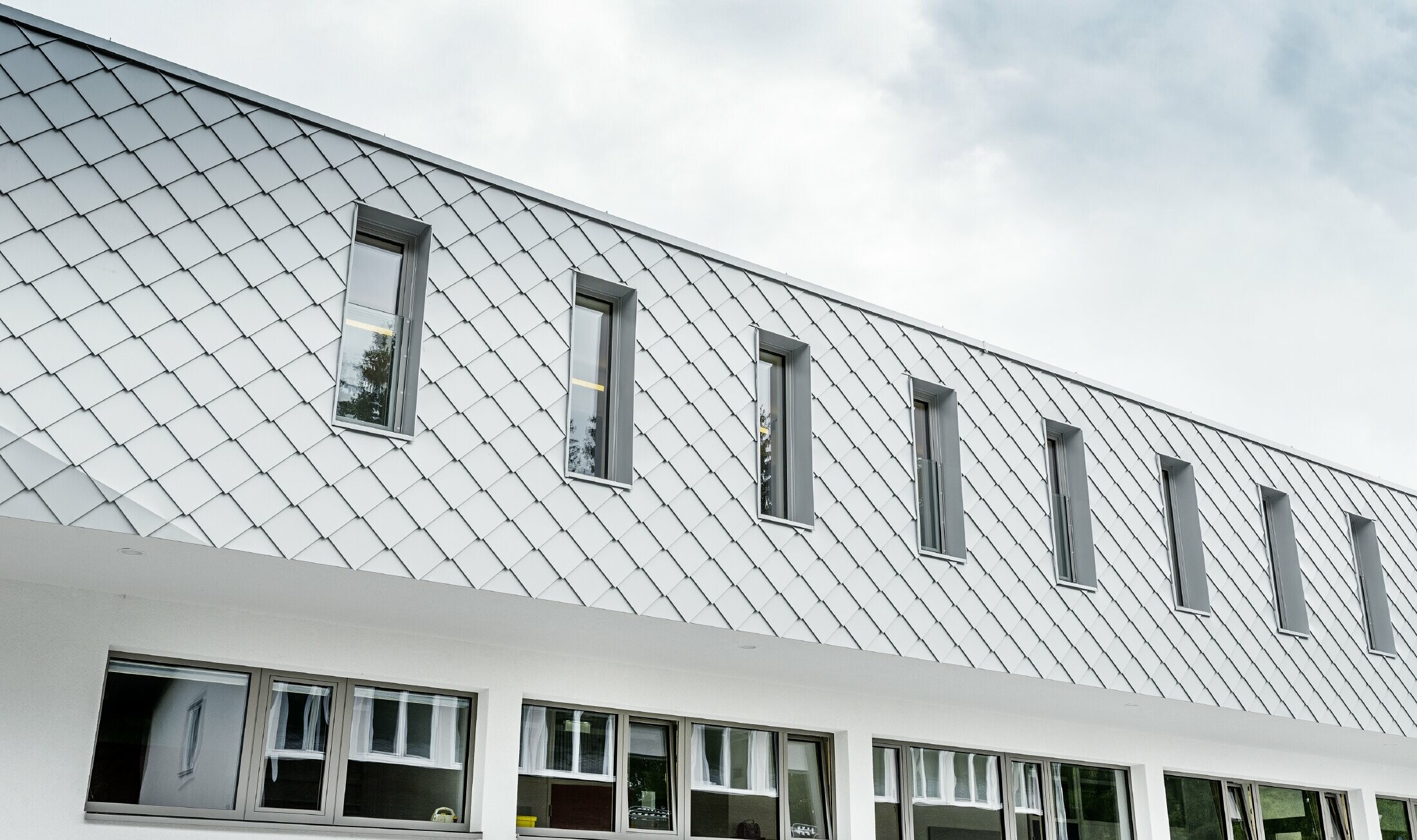 Scuola materna di nuova costruzione a Kaprun con una moderna facciata in alluminio con la scaglia per facciata PREFA in bianco PREFA