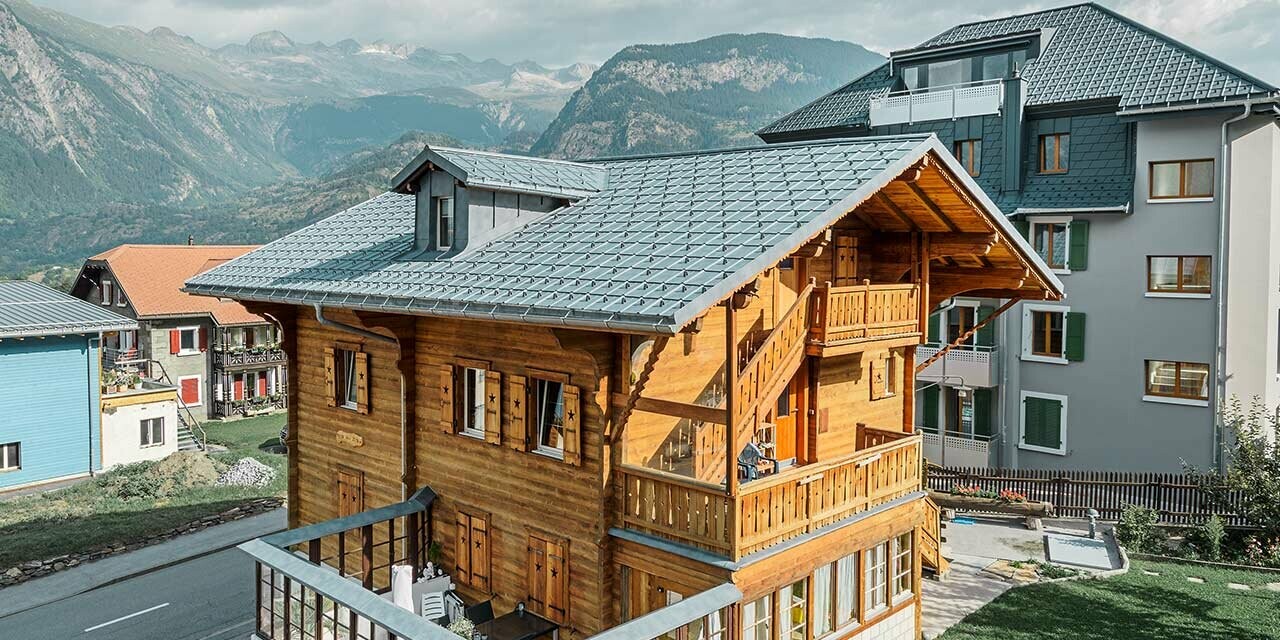 Chalet tradizionale svizzero in legno con abbaino e tetto a due falde; il tetto è rivestito con le classiche tegole PREFA in grigio pietra.