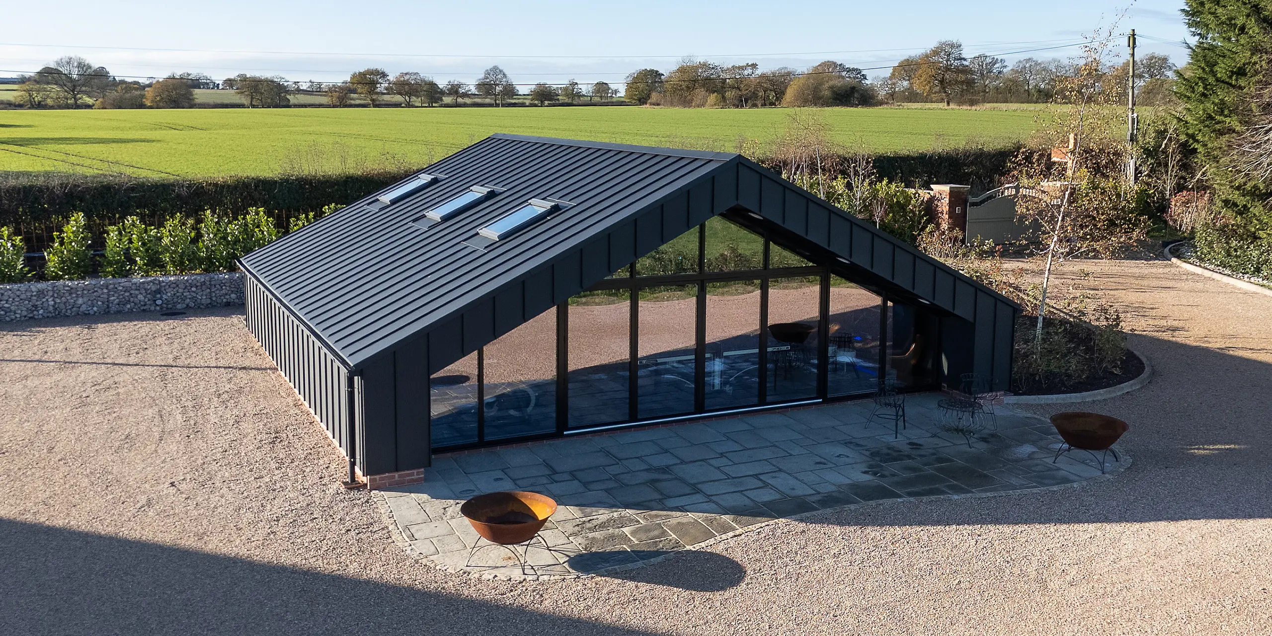 Vue aérienne d'un bâtiment de loisirs moderne entièrement revêtu d'aluminium PREFA et d'une toiture à joints debout PREFALZ P.10 noir. La forme symétrique du toit, la vaste façade vitrée et le patio extérieur bien délimité lui confèrent une présence architecturale remarquable. La surface en aluminium, durable et résistante aux intempéries, garantit une stabilité à long terme et une finition haut de gamme.