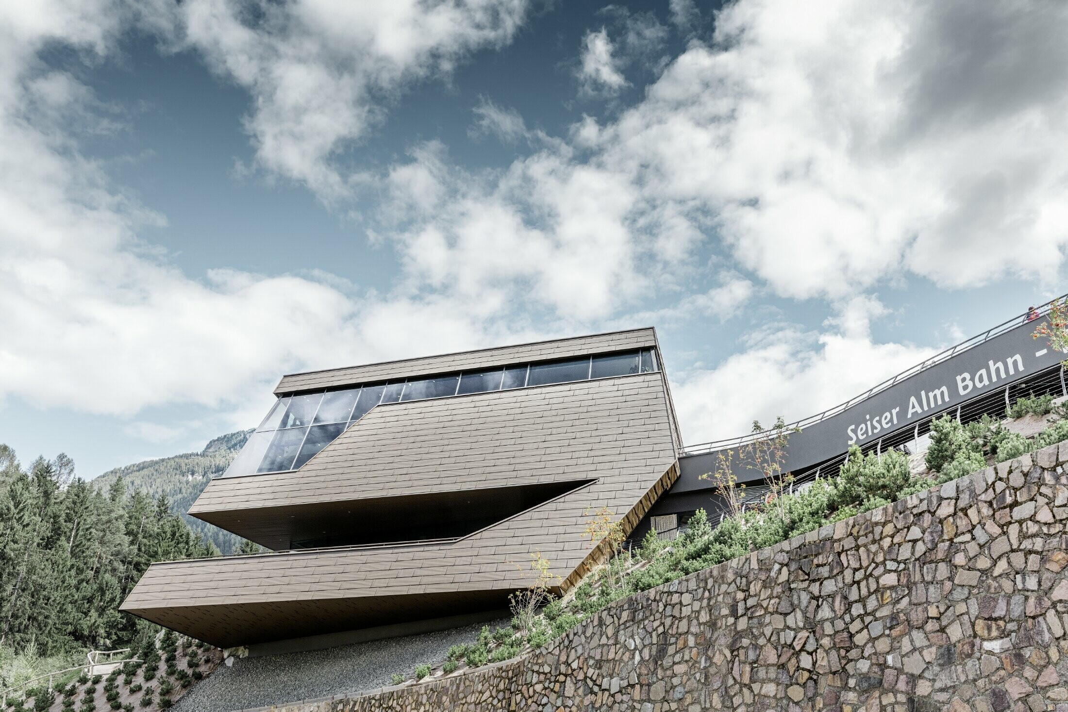 Gare de départ rénovée de la télécabine de l’Alpe di Siusi rappelant les Dolomites qui s’élèvent en toile de fond avec ses arêtes et ses surfaces irrégulières — Façade en aluminium PREFA (brun)