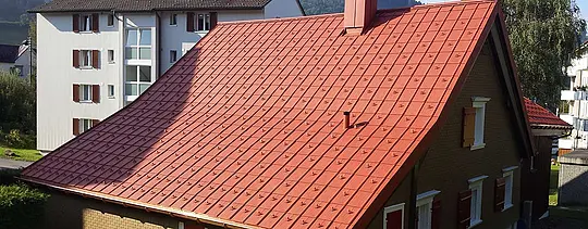 Satteldach mit der PREFA Dachplatte aus Aluminium eingedeckt. Dach in Ziegelrot mit Schneestoppern und Kamin