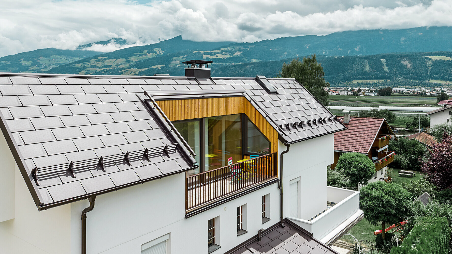 Bâtiment d’habitation recouvert de tuiles en aluminium R.16 couleur brun noisette de PREFA présentant un grand balcon et une façade en crépi clair.