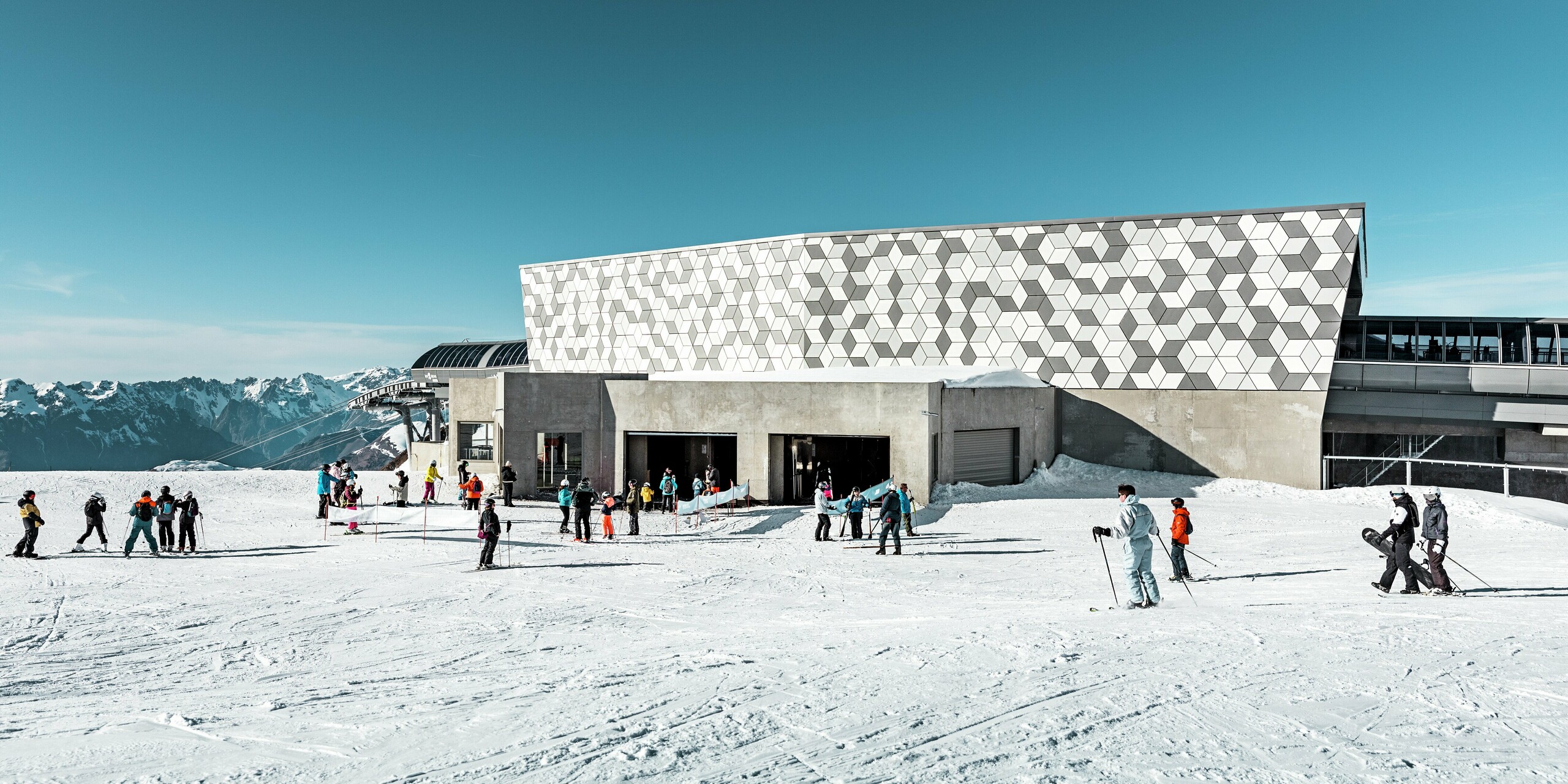 Die Mittelstation der 3S-Seilbahn in Les Deux Alpes sticht durch ihre moderne Fassade hervor. Die eindrucksvolle Gebäudehülle wurde mit PREFABOND Aluminium Verbundplatten in einem markanten Rautenmuster gestaltet. Die Kombination aus verschiedenen Weiß- und Grautönen ergänzt die schneebedeckte Umgebung perfekt. Der untere Teil des Gebäudes ist mit Sichtbeton ausgestattet. Die robusten und wetterfesten Materialien sehen nicht nur gut aus, sondern bieten auch langlebigen Schutz vor extremen Witterungsbedingungen.