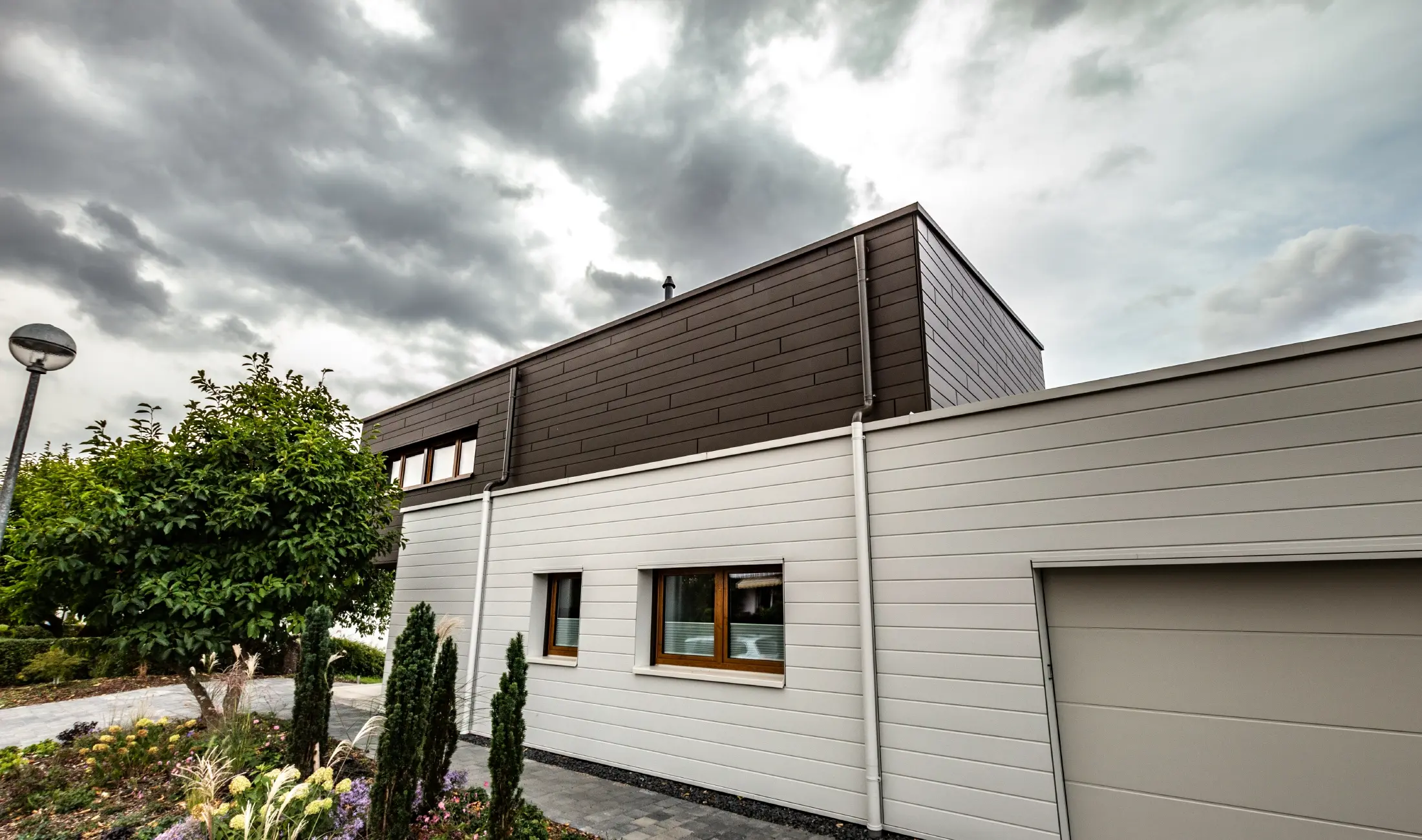 Rivestimento della facciata di un garage con doghe PREFA orizzontali di colore bianco, con grondaia con sbocco.