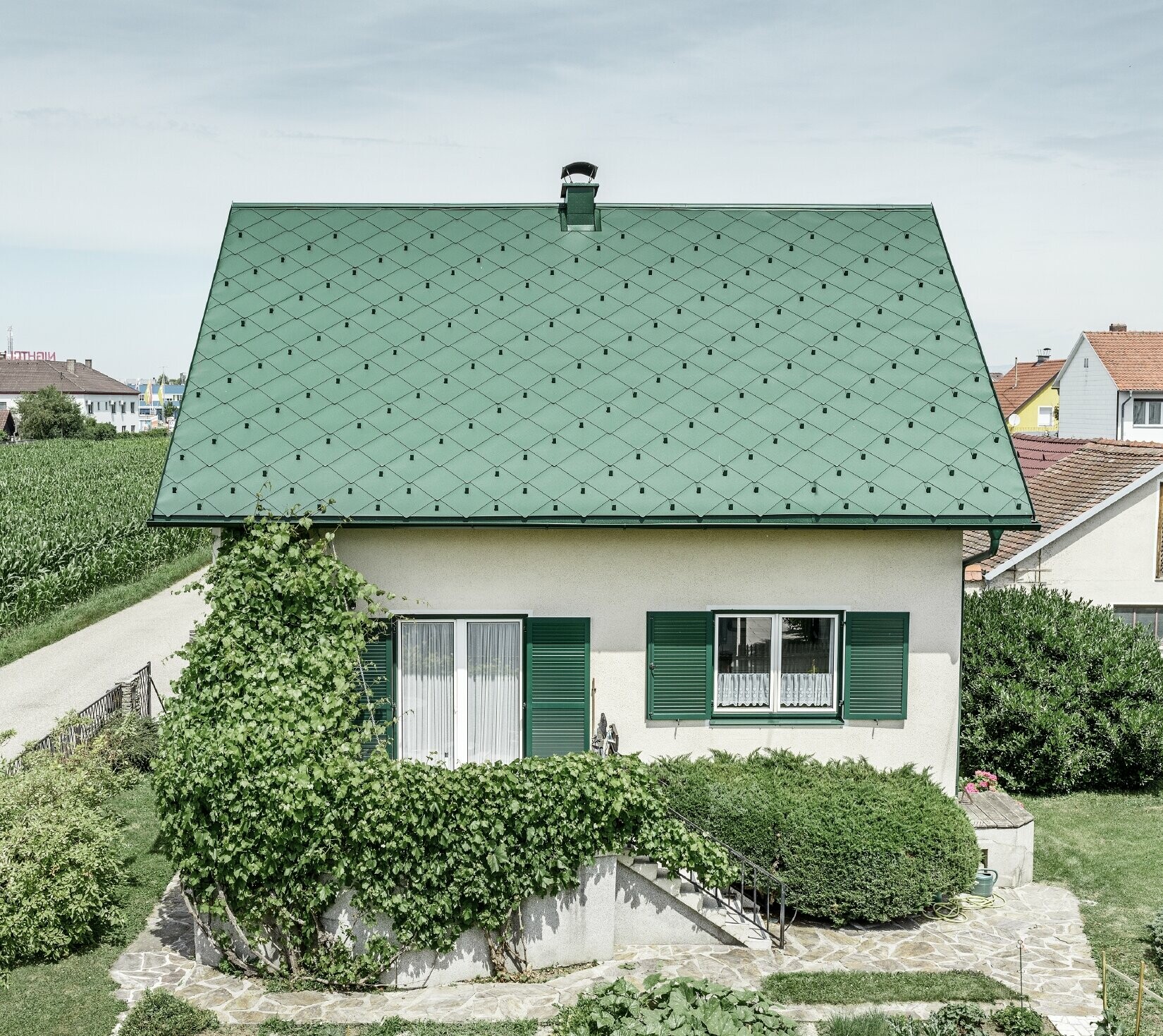 Klassisches Einfamilienhaus mit Satteldach mit einer Dacheindeckung aus Aluminium von in moosgrün mit grünen Fensterläden. Das Dach wurde mit PREFA Dachrauten 44 × 44 in P.10 Moosgrün eingedeckt.