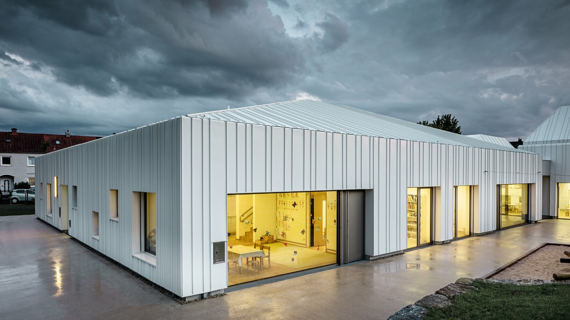 Crèche à Niederwerrn avec toit et façade PREFALZ dans la couleur blanc pur, avec différentes largeurs de bac, photographiée au crépuscule dans des conditions nuageuses