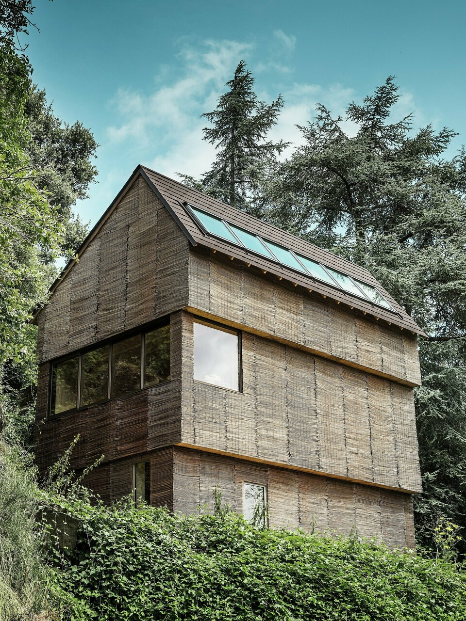 Ein Haus im Westen Frankreichs mit PREFA-Dachschindeln in der Farbe P.10 Walnussbraun, gelegen an einem steilen Hang – ein modernes Design mit einer Fassade aus Weidenholz und einem energieeffizienten Dach.