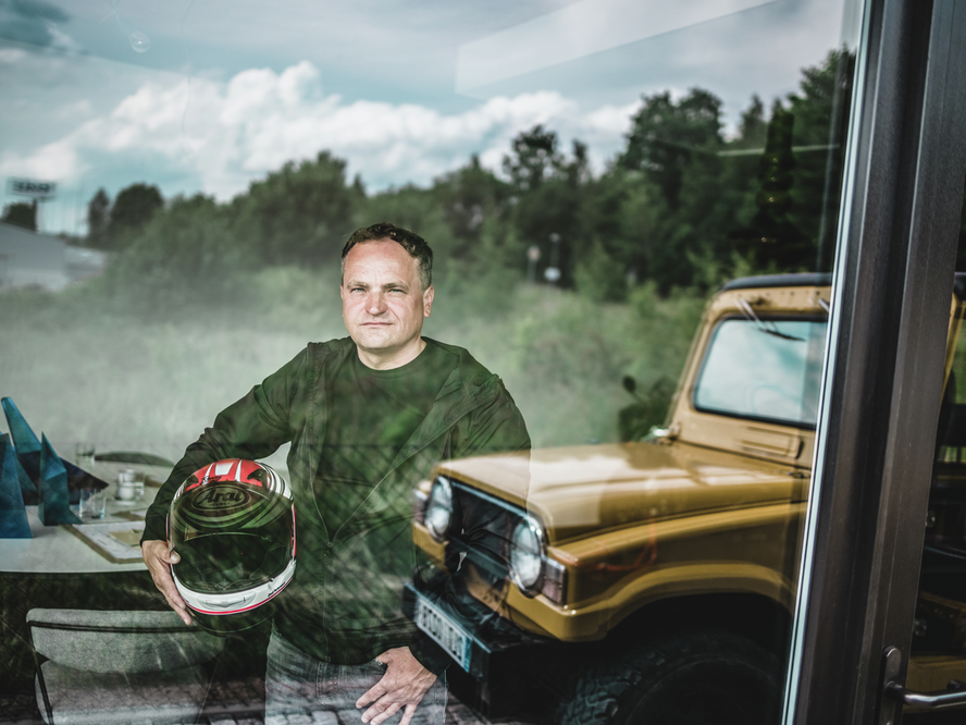 Un portrait de l'architecte Daniel Zerzan. Il tient un casque de moto à la main, et un pick-up jaune est également visible.