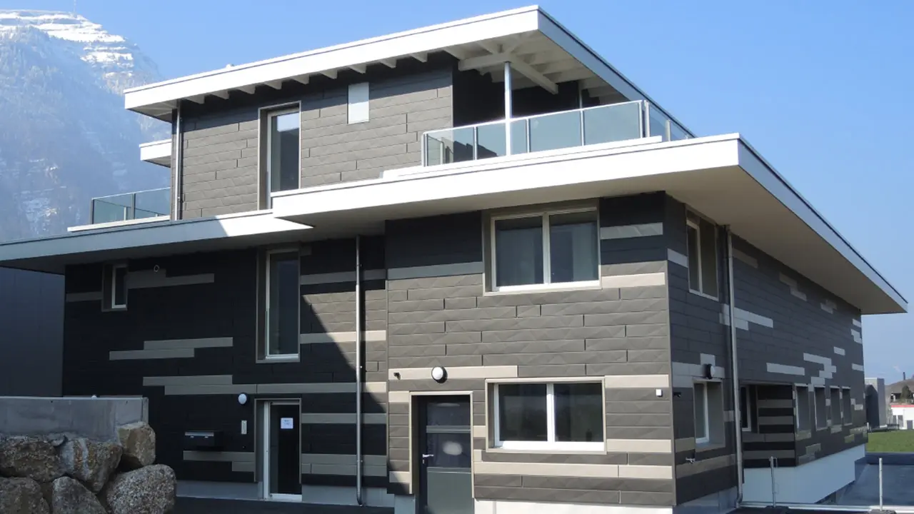 Modernes Gebäude in der Schweiz mit Bergen im Hintergrund mit einer neuen PREFA Siding.X Fassade; Die Alu-Paneele wurden in zwei unterschiedlichen Farben montiert, daraus ergibt sich ein individuelles Fassadendesign.
