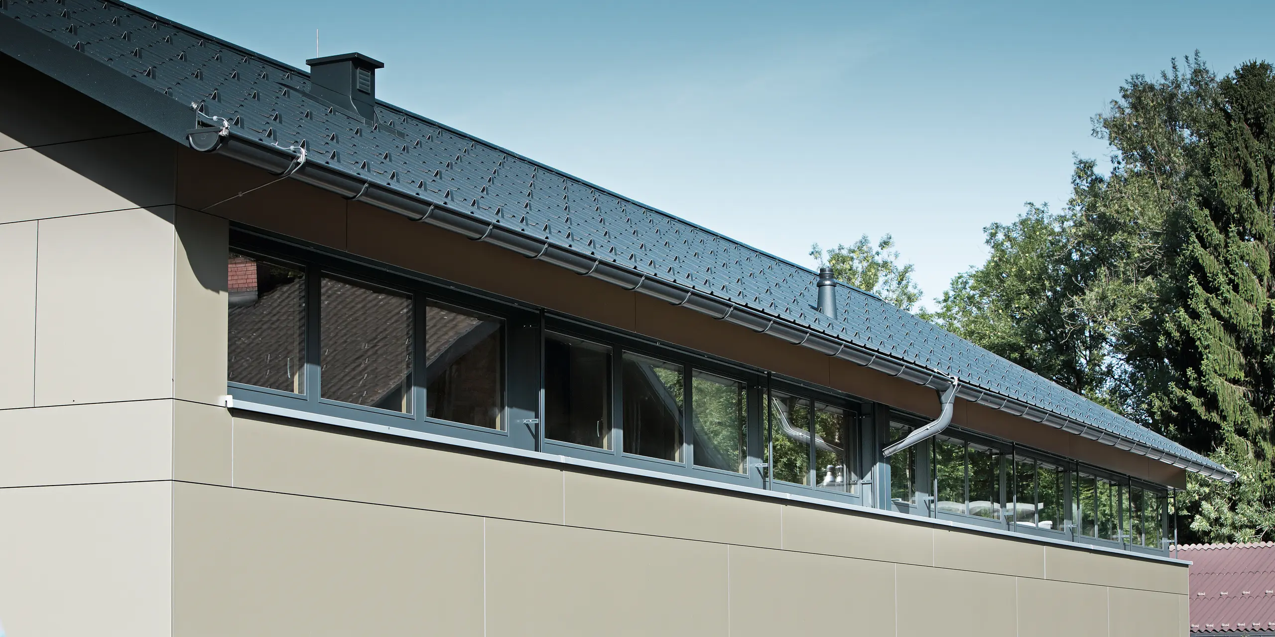 Obergeschoss eines Einfamilienhauses in Hohenems, ausgestattet mit einem langlebigen PREFA Komplettsystem. Die sichtbare Aluminium Verbundplatte in Bronzemetallic schafft eine glatte und moderne Fassade, die in Einklang mit den großflächigen Fenstern steht. Die PREFA Dachplatten in P.10 Anthrazit unterstreichen die Hochwertigkeit der Baumaterialien und die anspruchsvolle Ästhetik des Hauses. Die Schneestopper am Dach sorgen zudem für notwendige Sicherheit in den Wintermonaten.