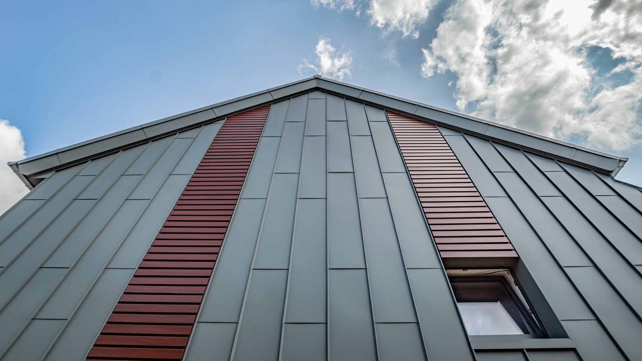 Vertikale Winkelstehfalzfassade mit Tafeldeckung in Hellgrau, sowie Siding horizontal in Holz dunkel von PREFA.