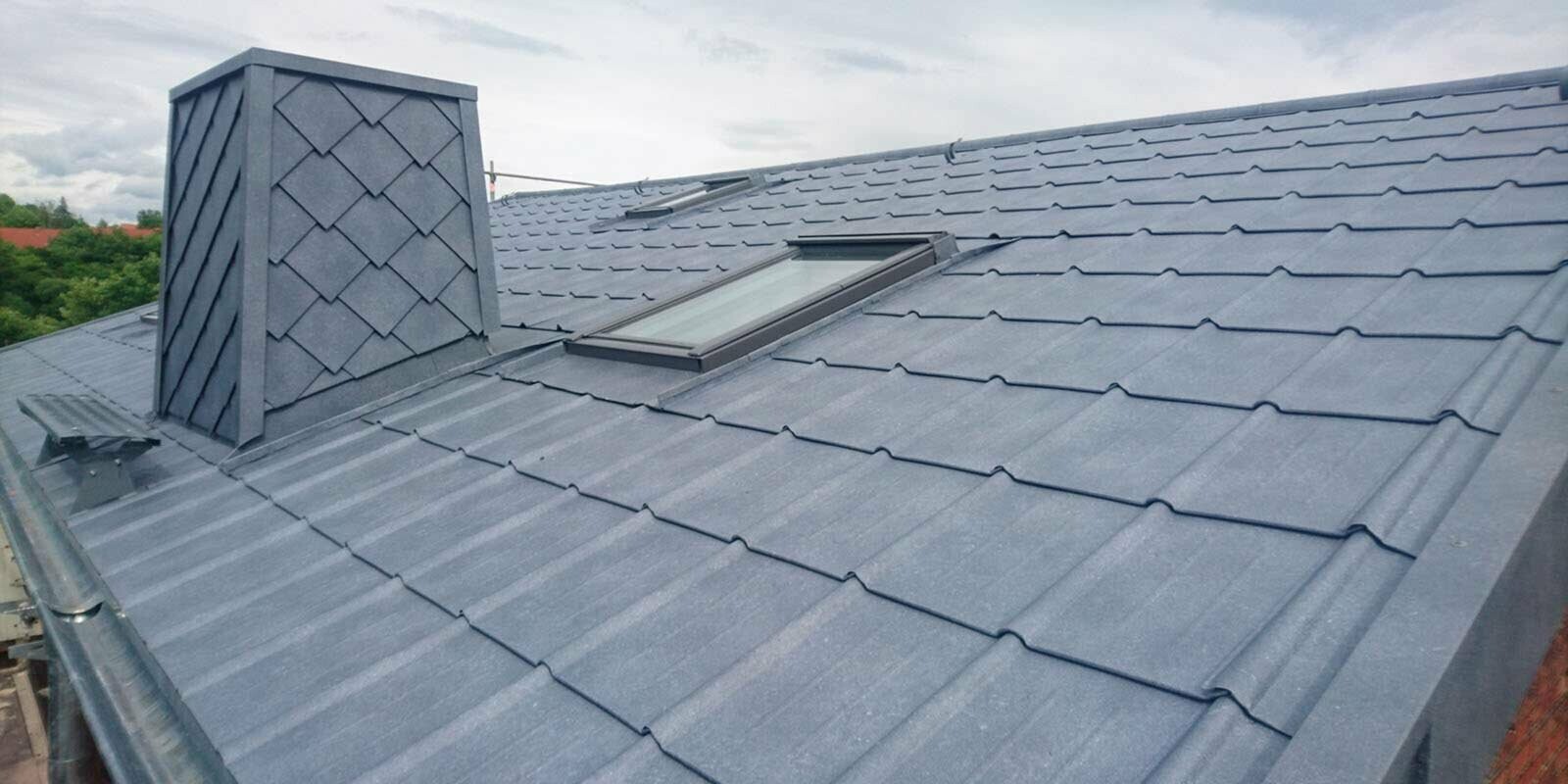 Vue détaillée d’une rénovation de toiture à l’aide de tuiles PREFA couleur P.10 gris pierre, habillage de la cheminée inclus