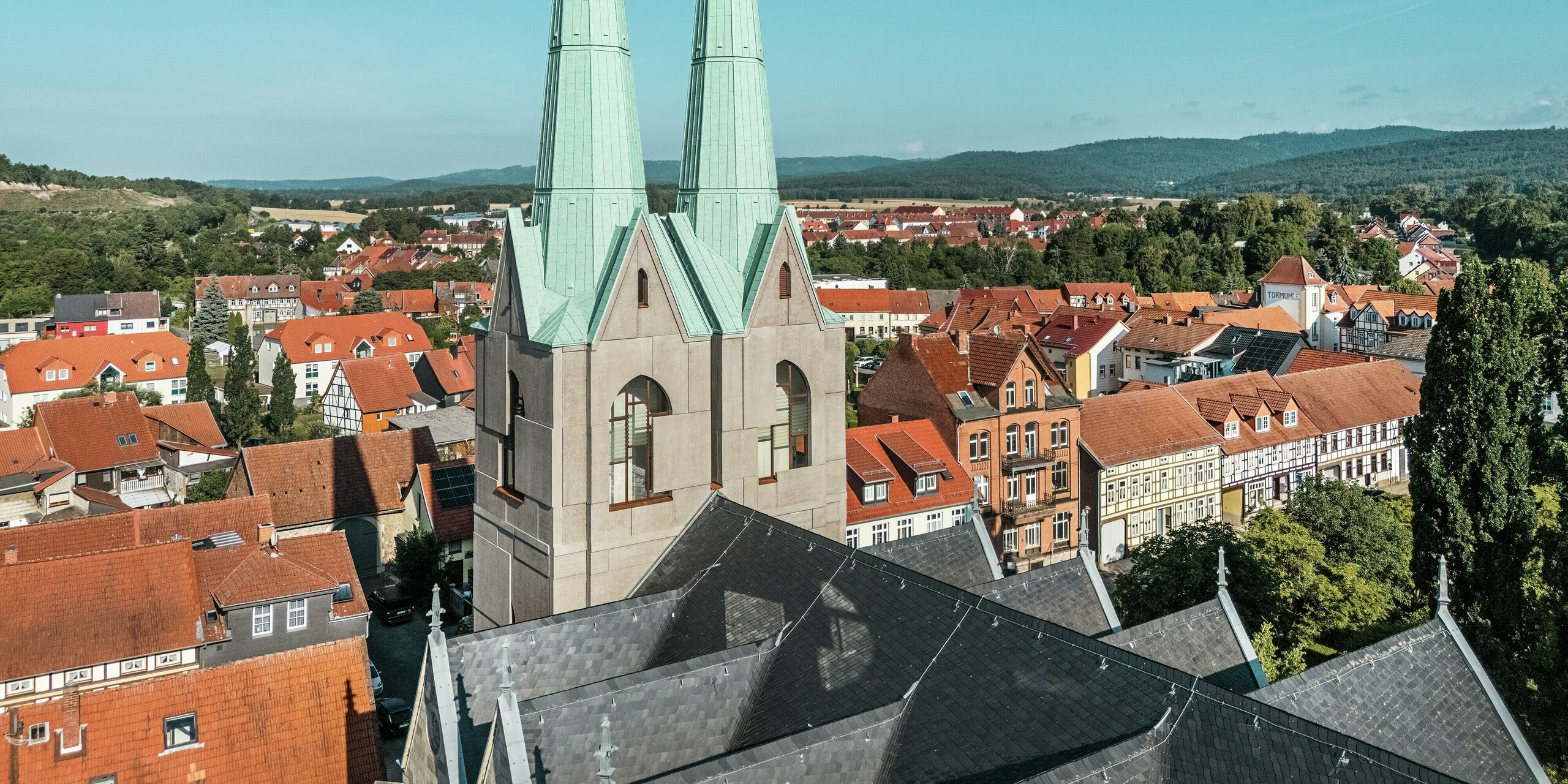 Images aériennes des flèches nouvellement conçues de l'église Saint-Jean d'Ellrich, qui se détachent avec élégance sur le paysage urbain grâce au revêtement PREFALZ vert de gris P.10. Les lignes épurées et la toiture moderne en aluminium s'harmonisent avec le cadre historique tout en offrant une résistance maximale aux intempéries, une grande durabilité et un design raffiné.