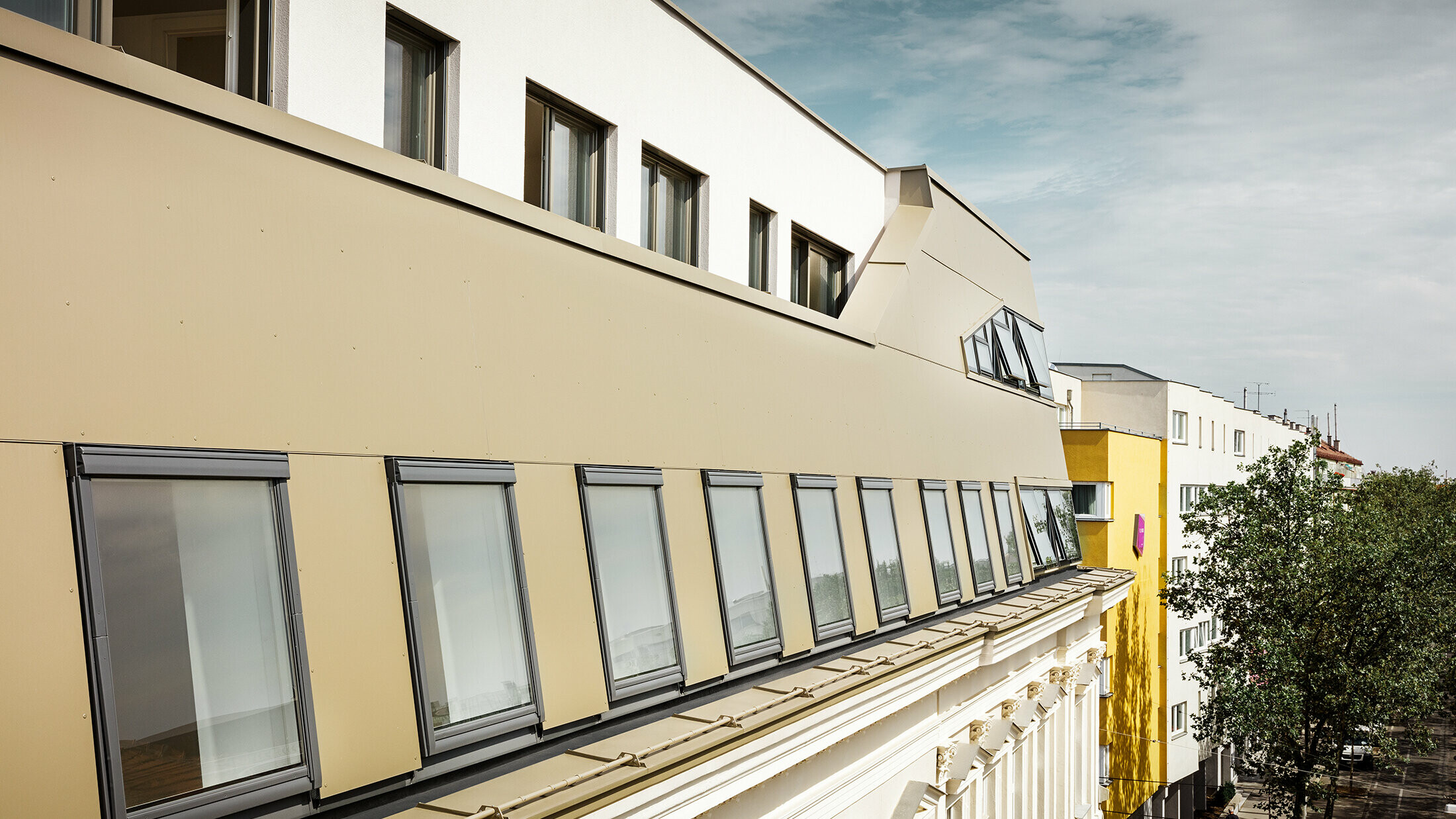 Die seitliche Ansicht des Dachgeschosses hebt die gleichmäßige Verkleidung mit PREFA Aluminium Verbundplatten in Bronze hervor. Große Fenster und flächige Glaselemente sorgen für lichtdurchflutete Räume und ein elegantes, modernes Erscheinungsbild.